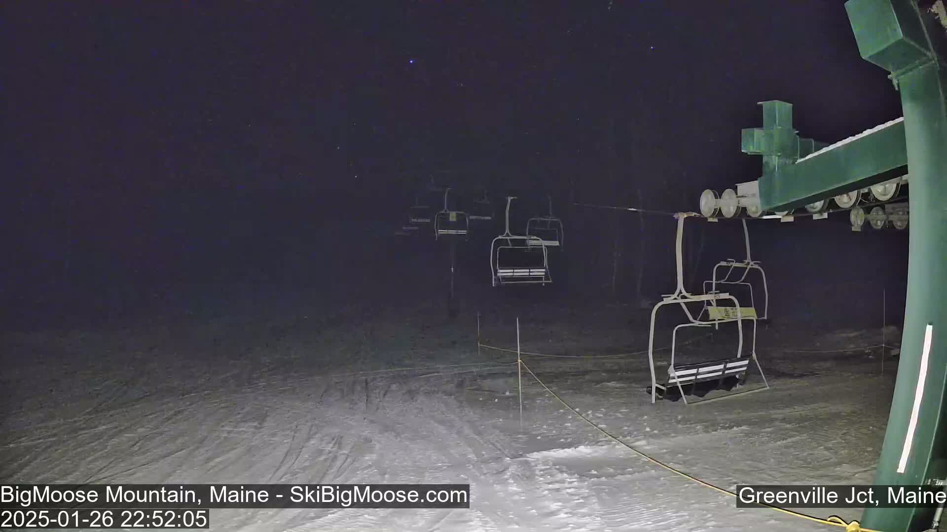 Under a dark, nighttime sky, a snow-covered ski lift stands empty at the base of a ski slope.
