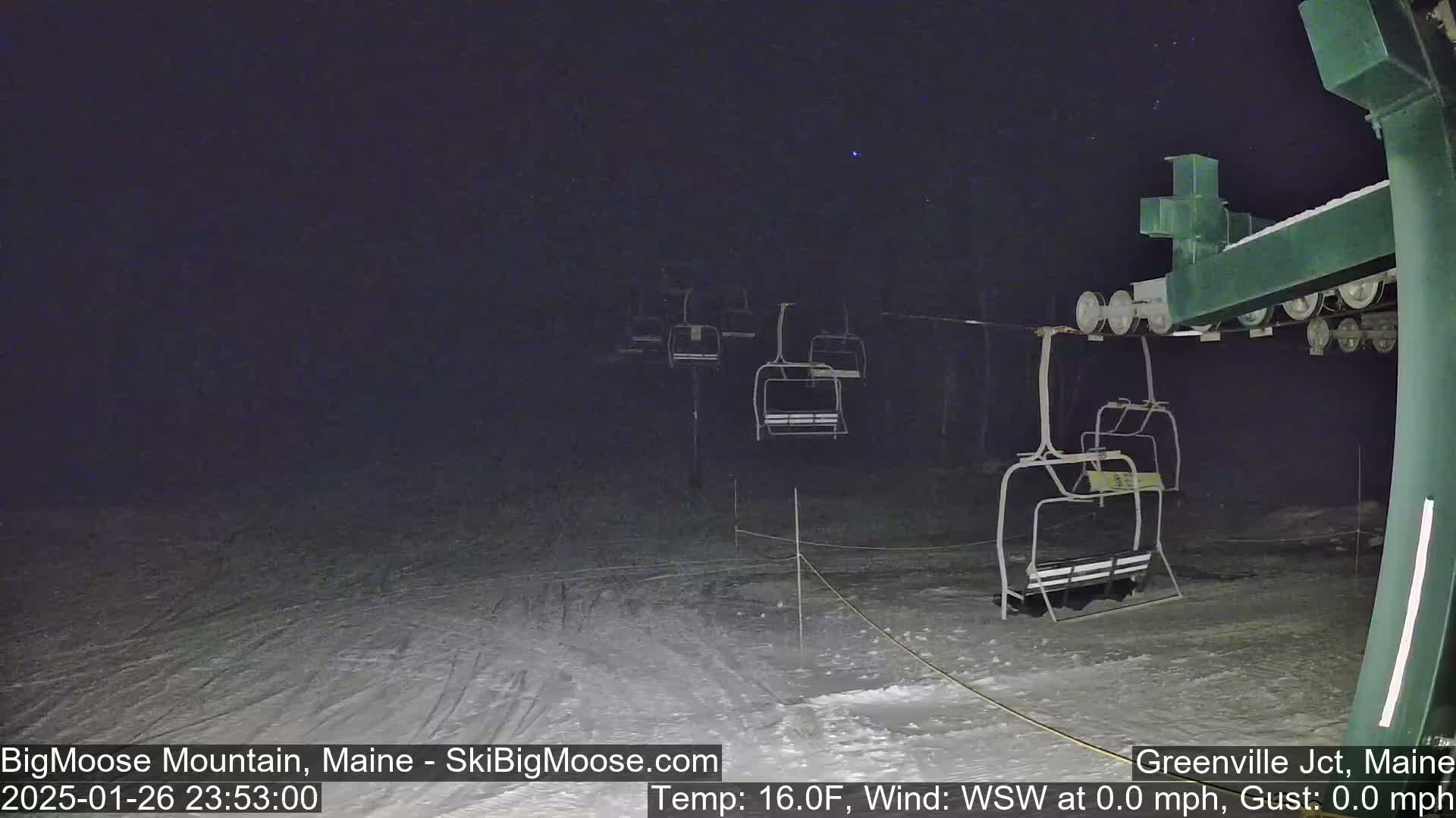 A nighttime view of a ski lift with several empty chairlifts on a snow-covered slope under a clear, dark sky.