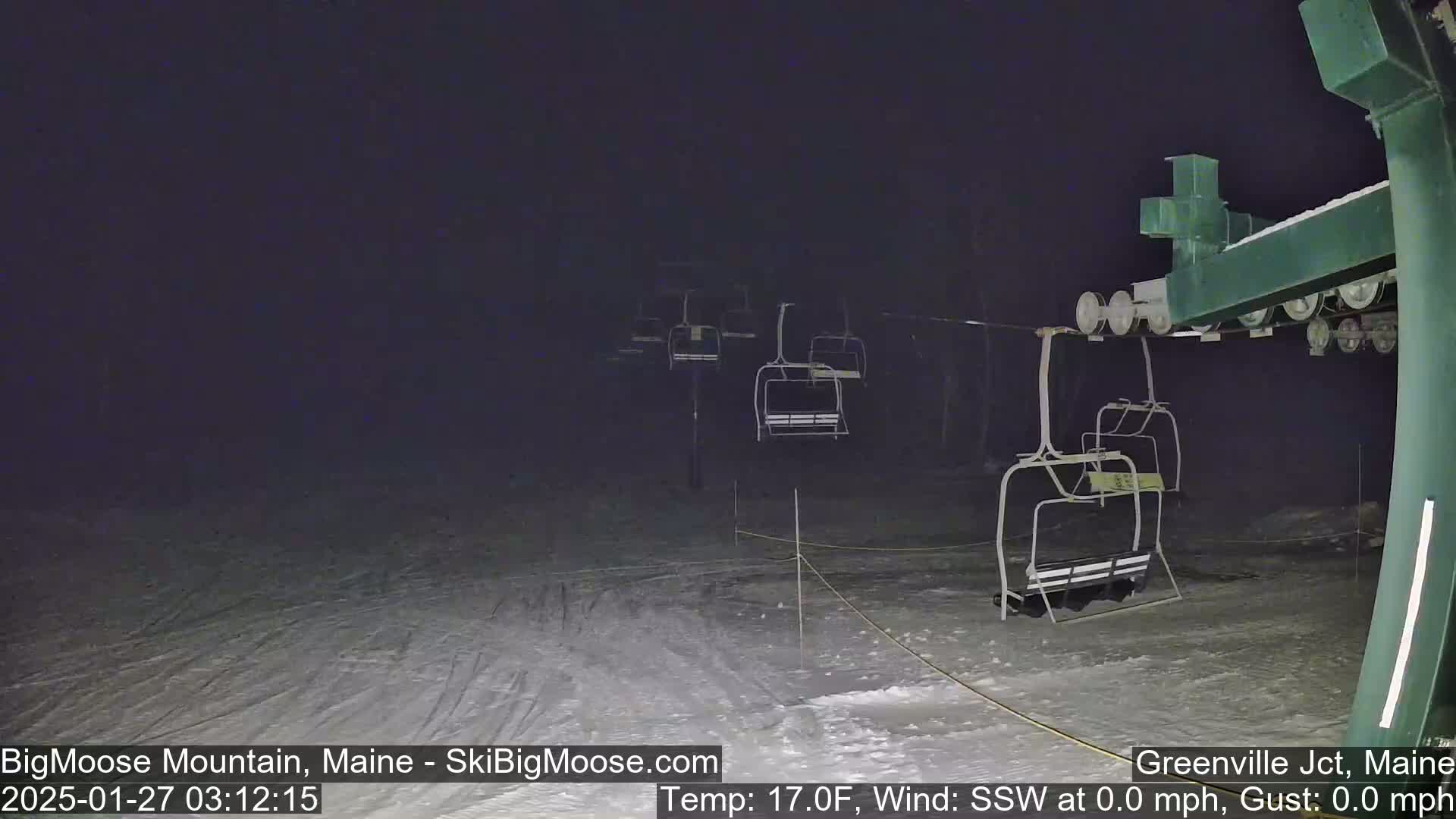A nighttime view of a ski lift at a snow-covered ski resort under a dark, clear sky.
