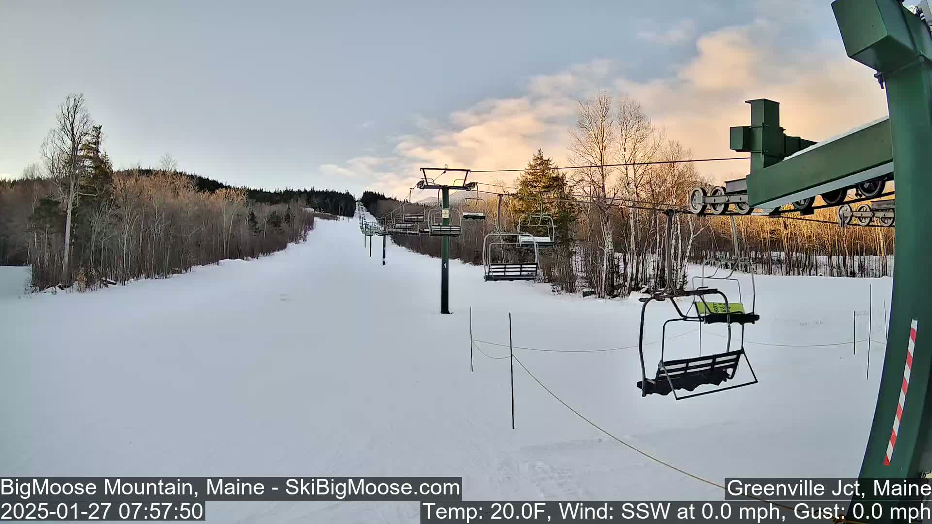 A snow-covered ski slope with a chairlift under a partly cloudy, twilight sky.