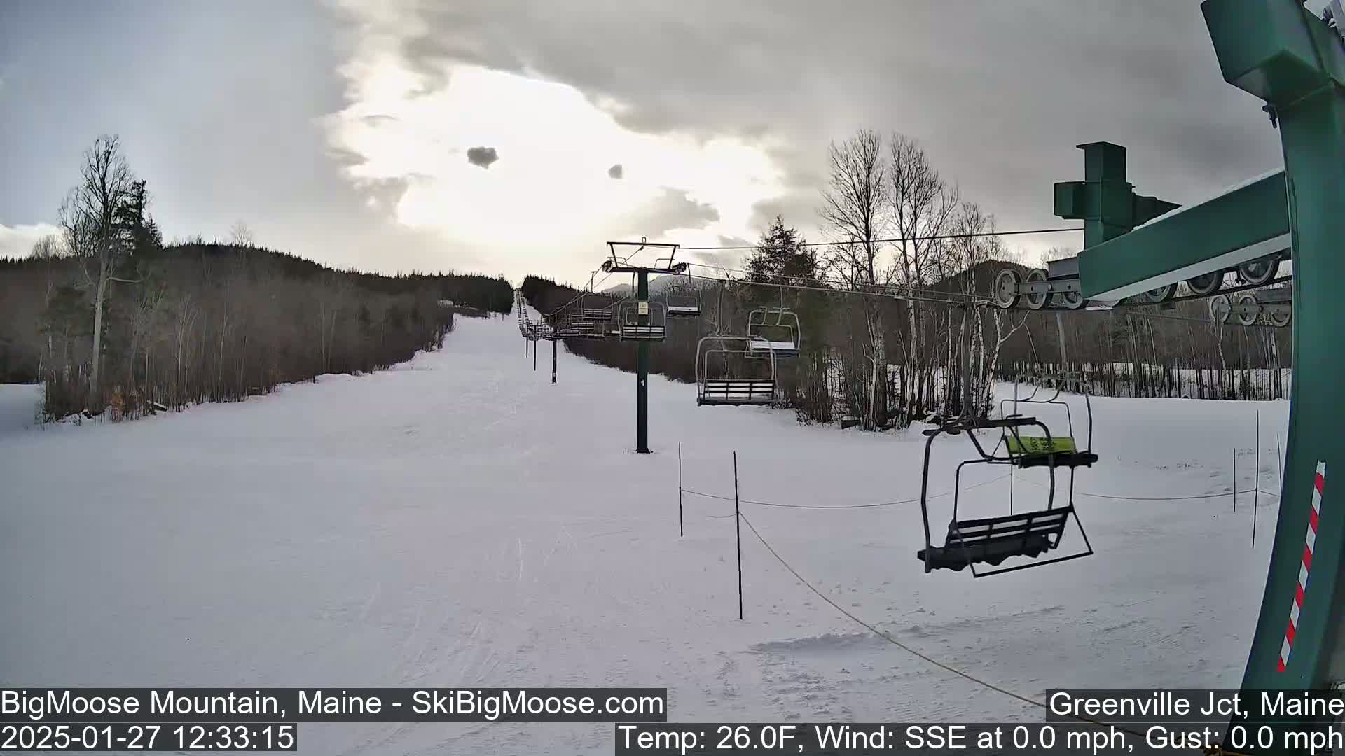 A ski lift ascends a snow-covered hill under a partly cloudy sky.