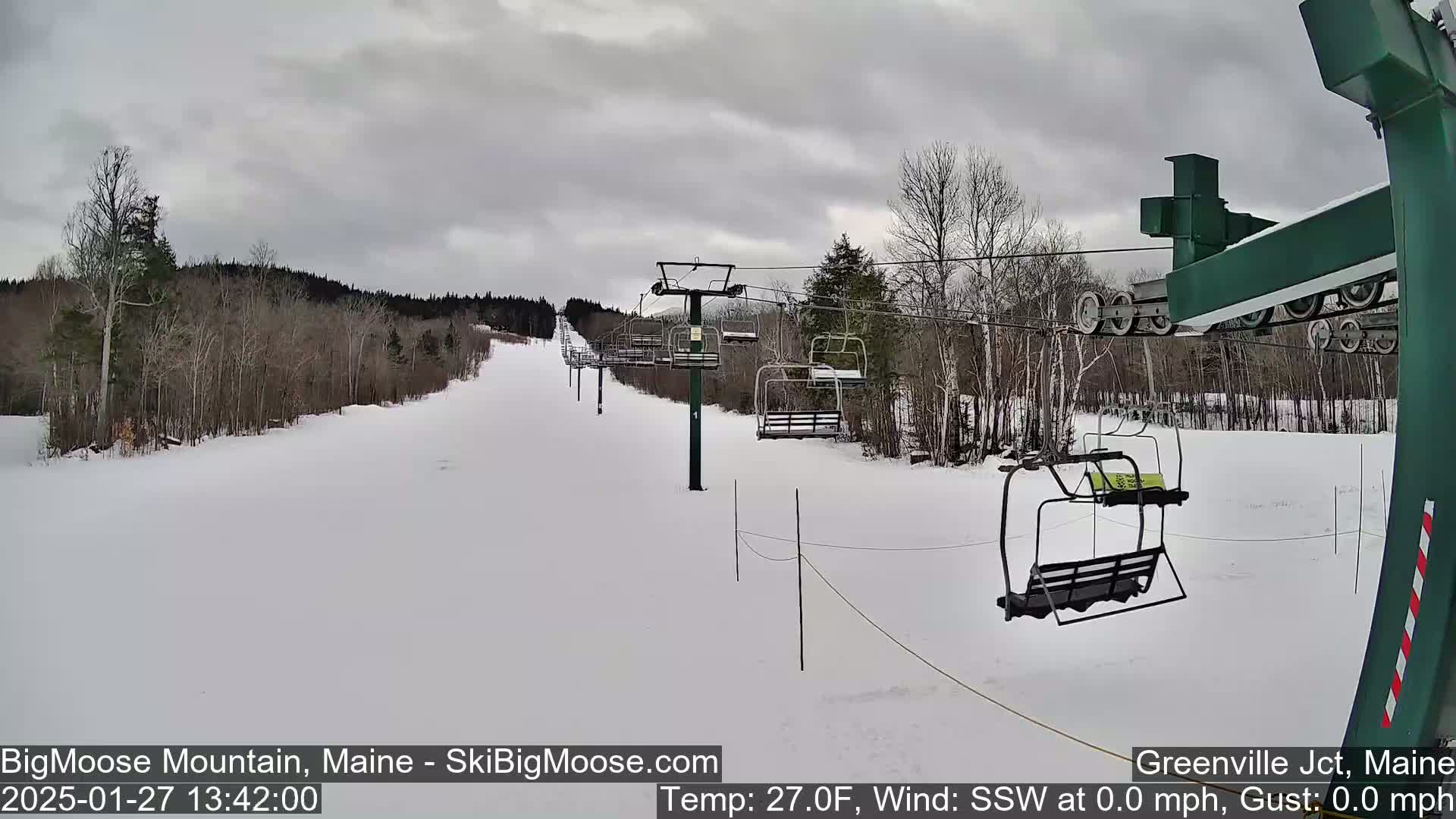 A snow-covered ski slope with a chairlift and leafless trees under an overcast sky.
