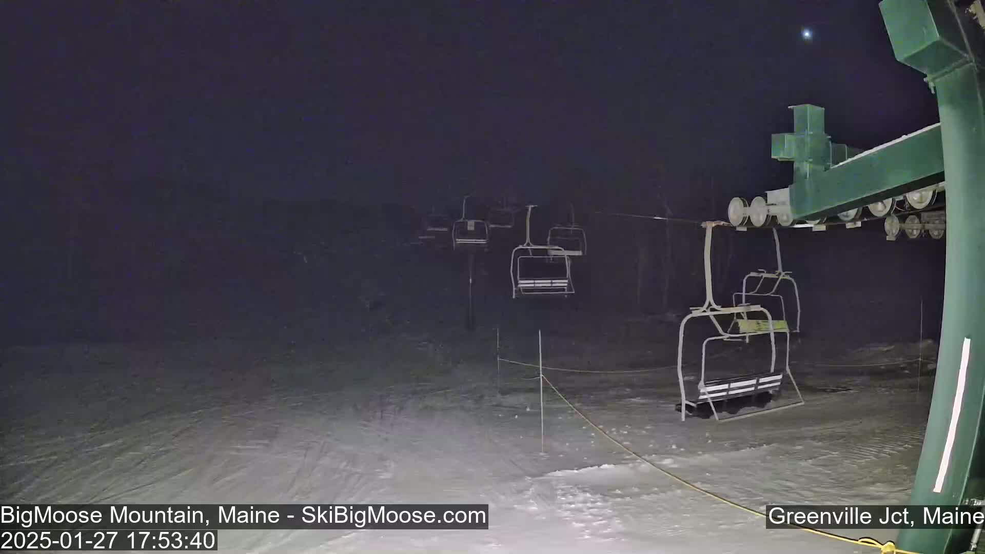 A nighttime view of a ski lift with several empty chairlifts under a dark, clear sky.