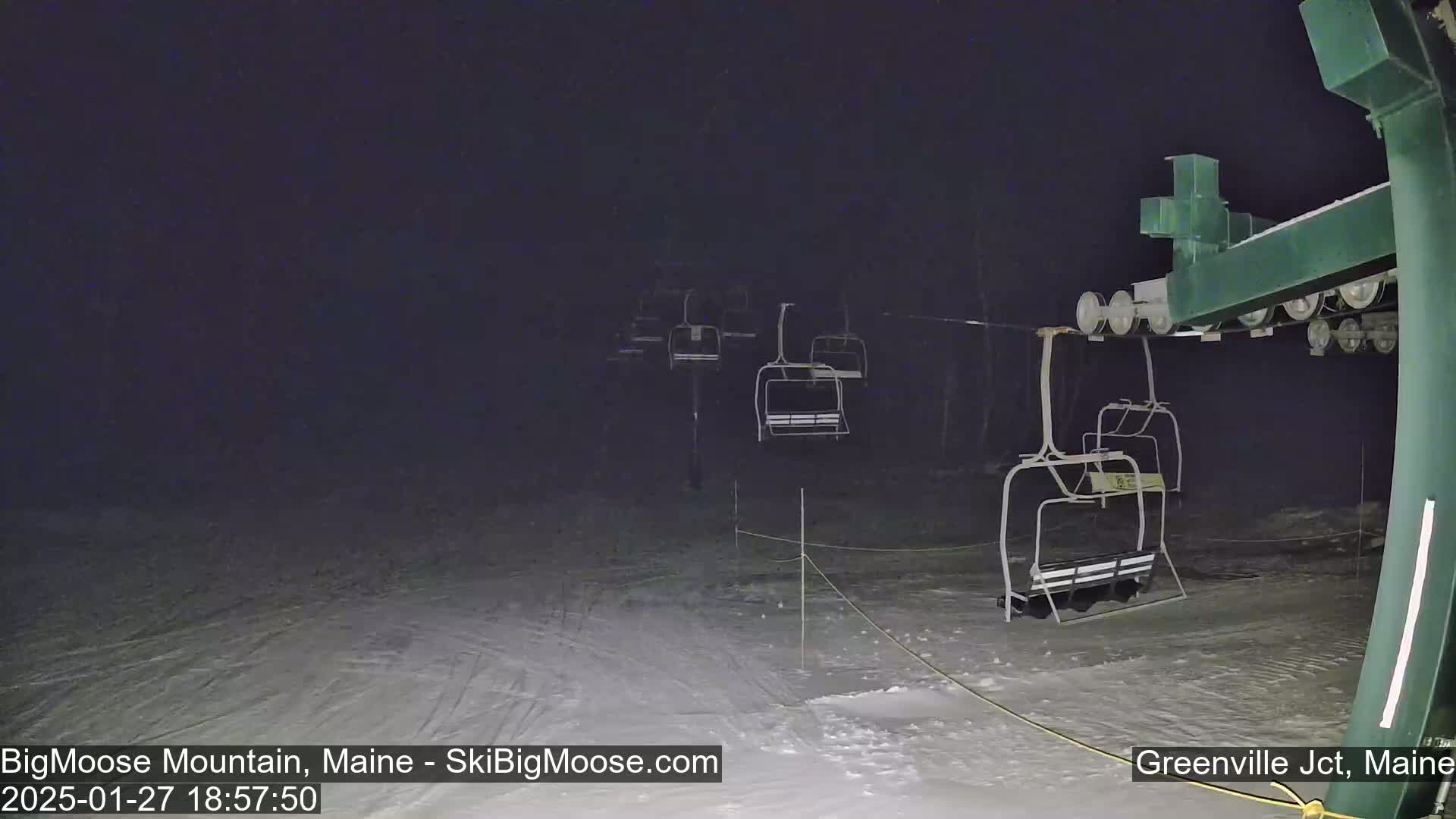 A nighttime view of empty chairlifts on a snow-covered ski slope under dark, cloudy conditions.