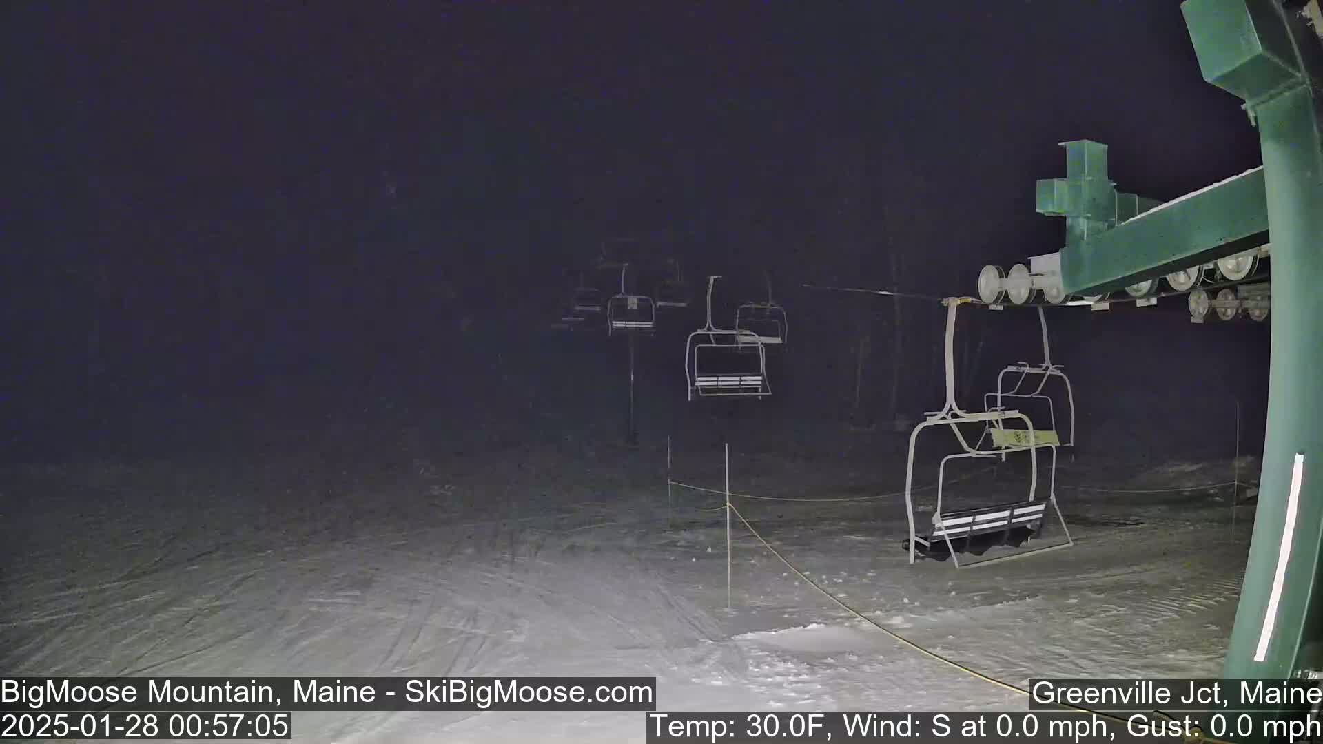 A nighttime view of a snow-covered ski lift with several empty chairlifts under a dark sky.