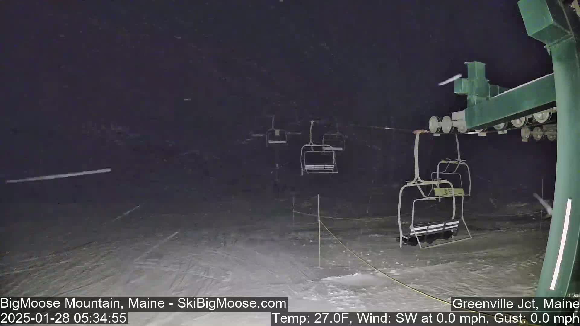 A nighttime view of a ski lift with several empty chairs under light snowfall.