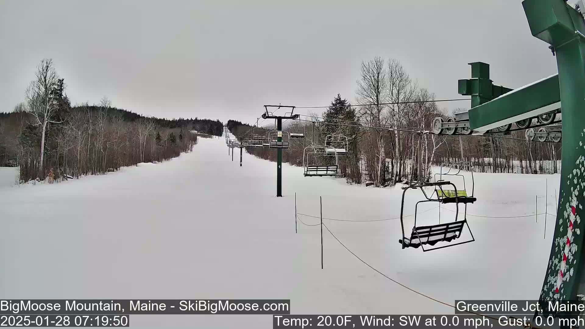 A snow-covered ski slope with a chairlift and sparsely wooded areas under an overcast sky.
