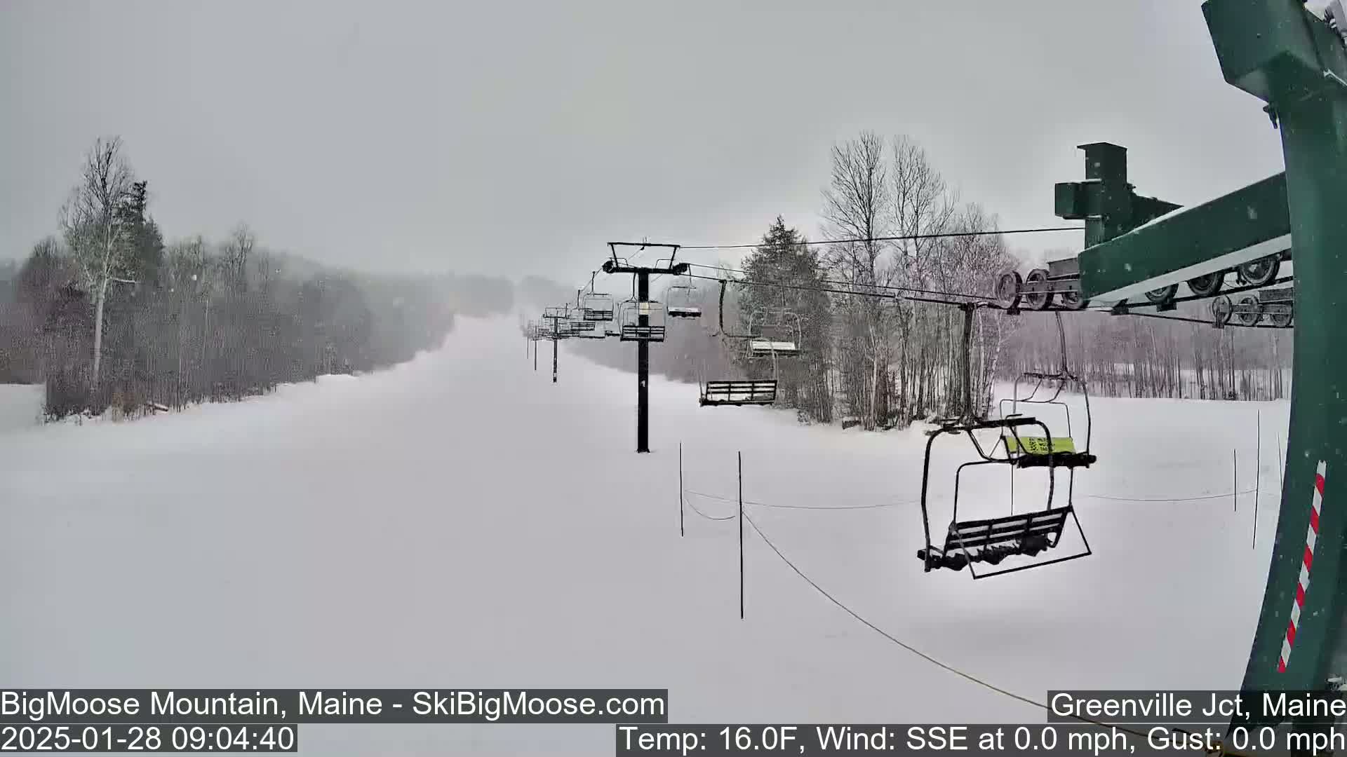 A snow-covered ski slope with a chairlift in operation during a light snowfall.