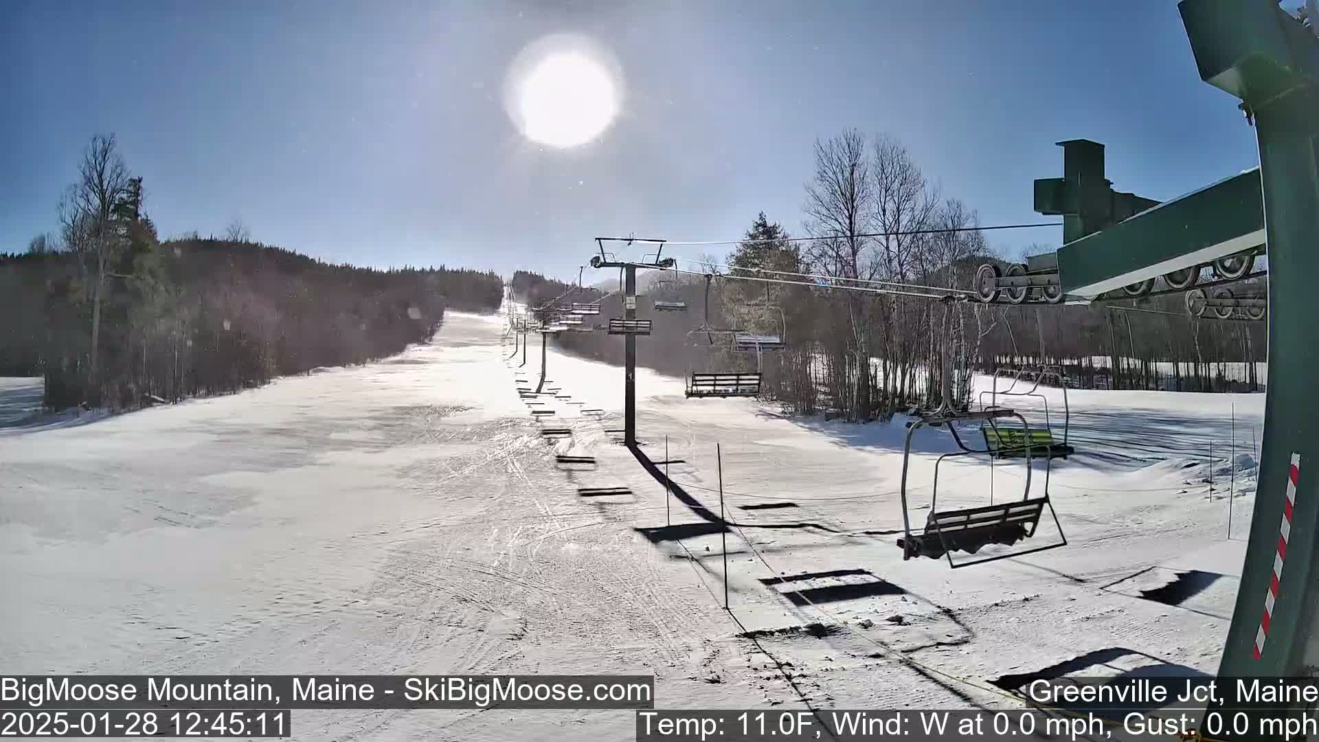 A sunny, snow-covered ski slope with a chairlift and several empty chairs.