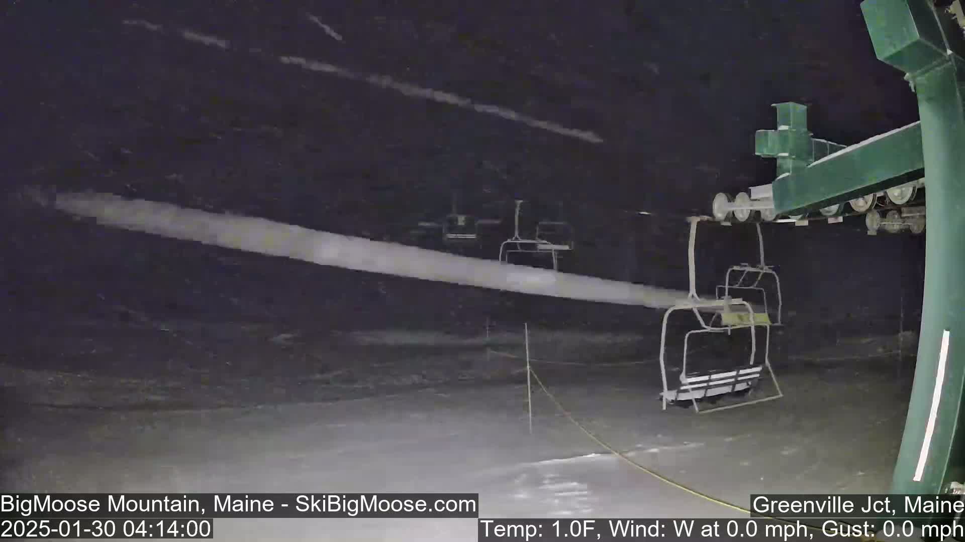 A snow-covered ski lift sits under a dark, nighttime sky with blowing snow.