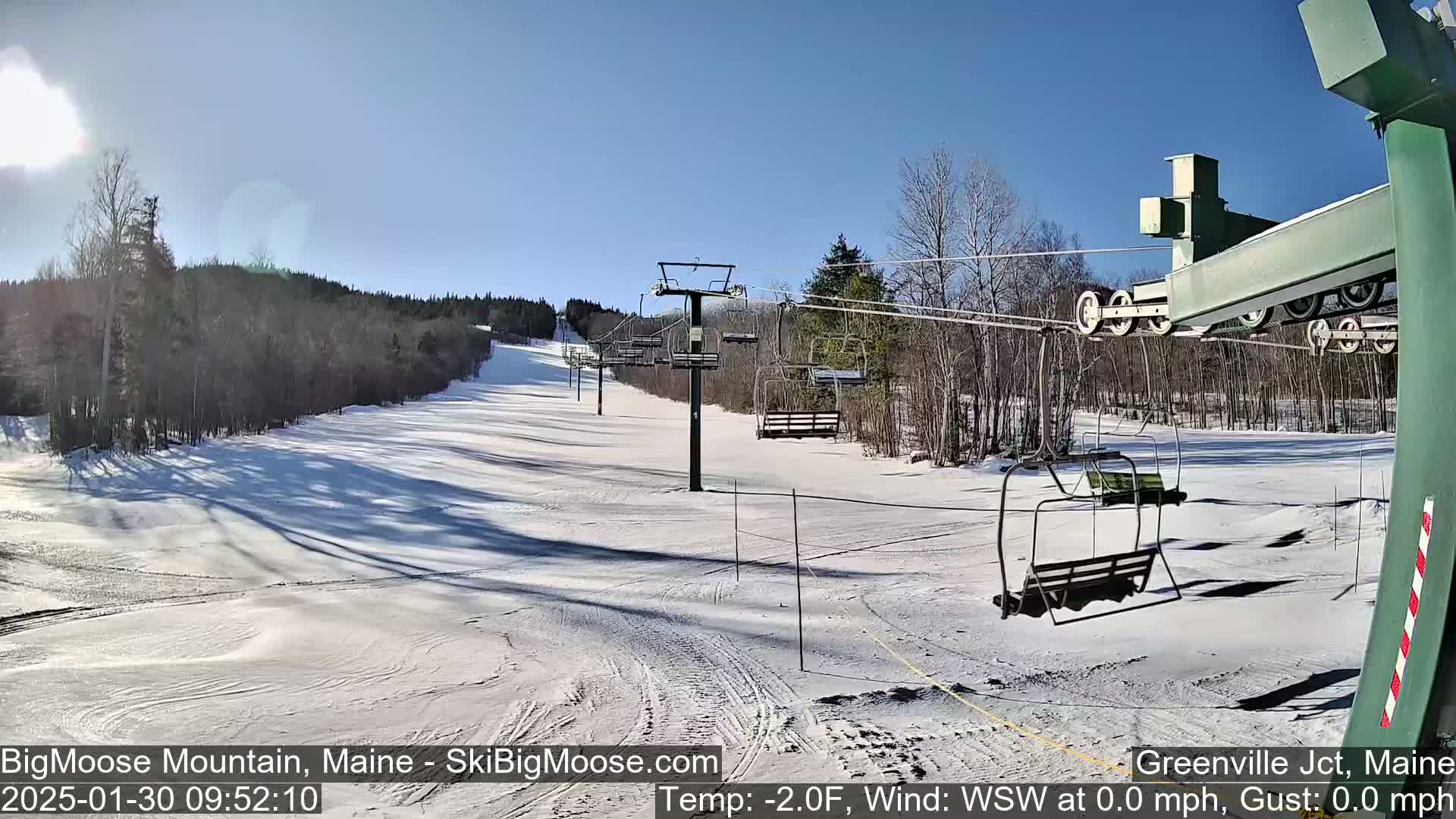 A sunny, snow-covered ski slope with a chairlift and trees in the background.