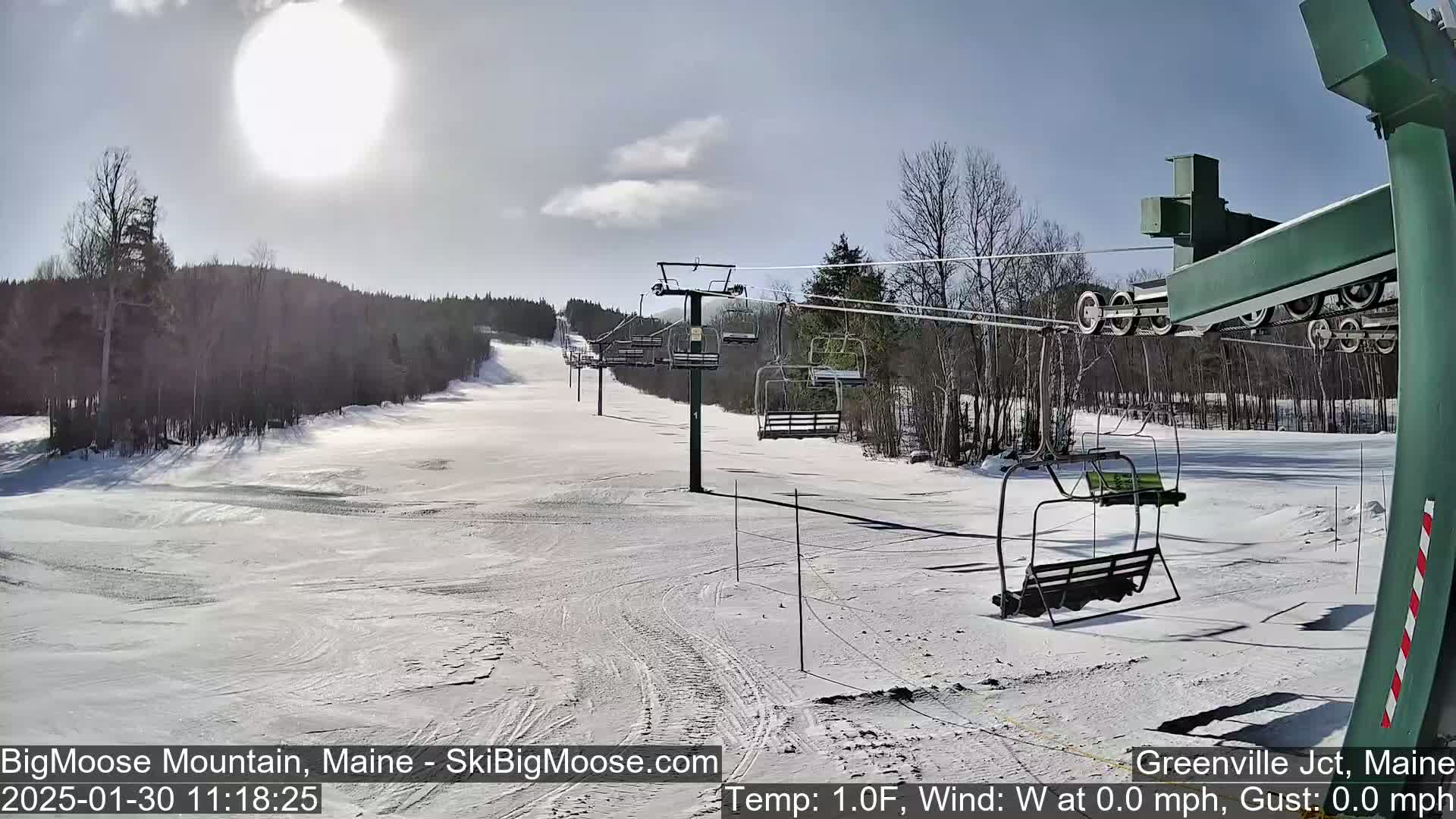 A sunny, snow-covered ski slope with a chairlift and surrounding trees.