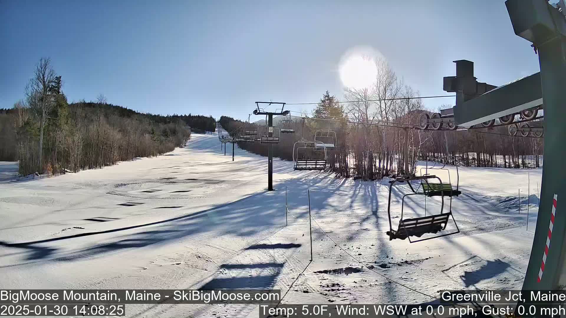 A sunny, snow-covered ski slope with a chairlift and surrounding trees.