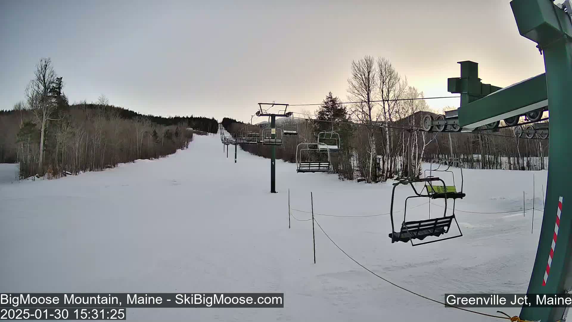 A ski lift with empty chairs ascends a snow-covered hill under a twilight sky.