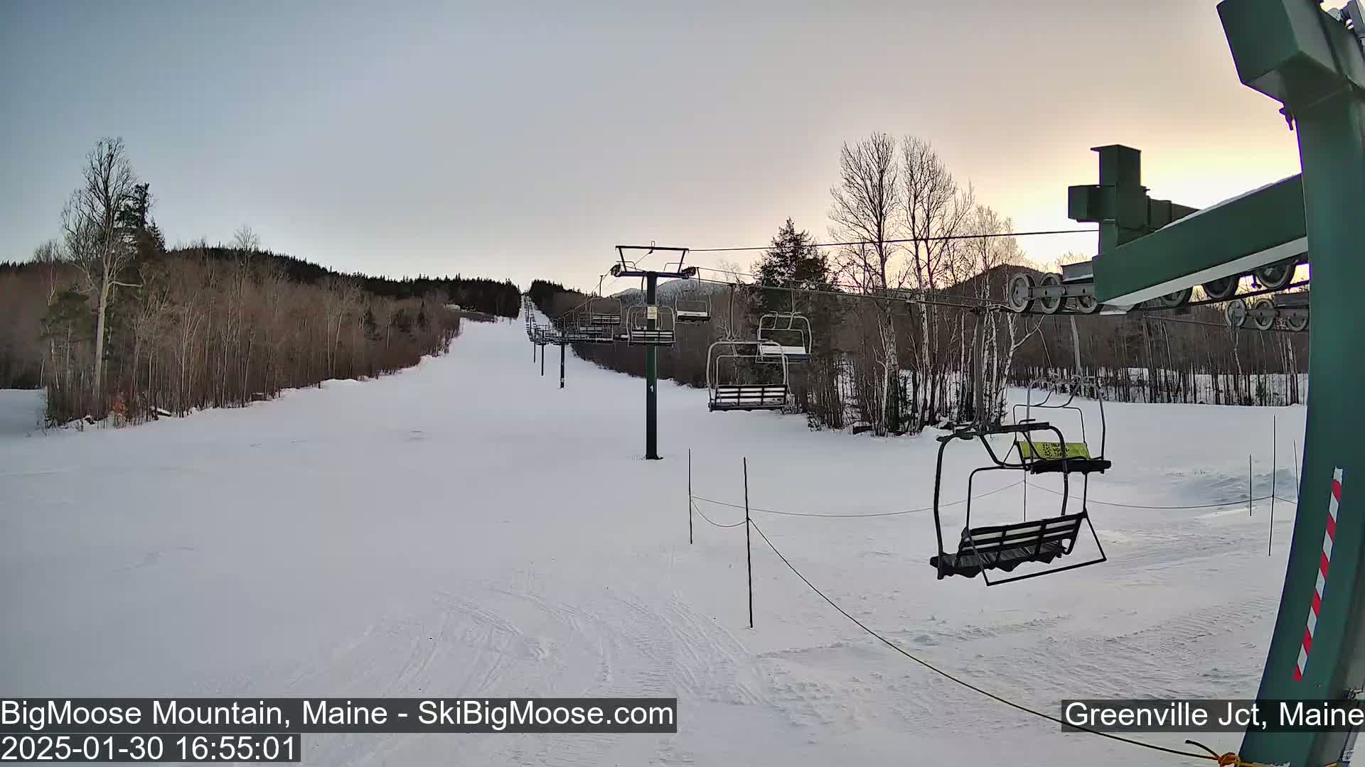 A snow-covered ski slope with a chairlift and bare trees under a twilight sky.