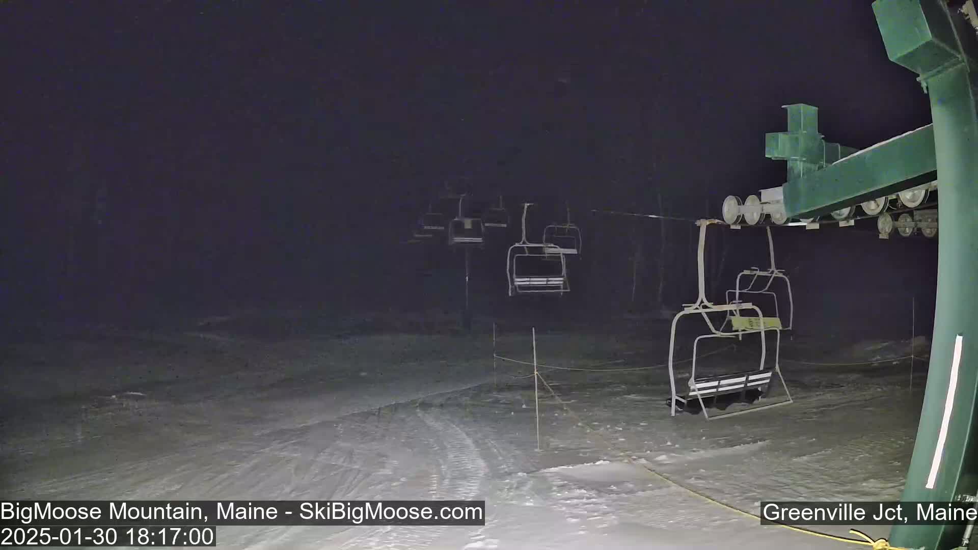 Under a dark night sky, several empty chairlifts are visible on a snow-covered ski slope.