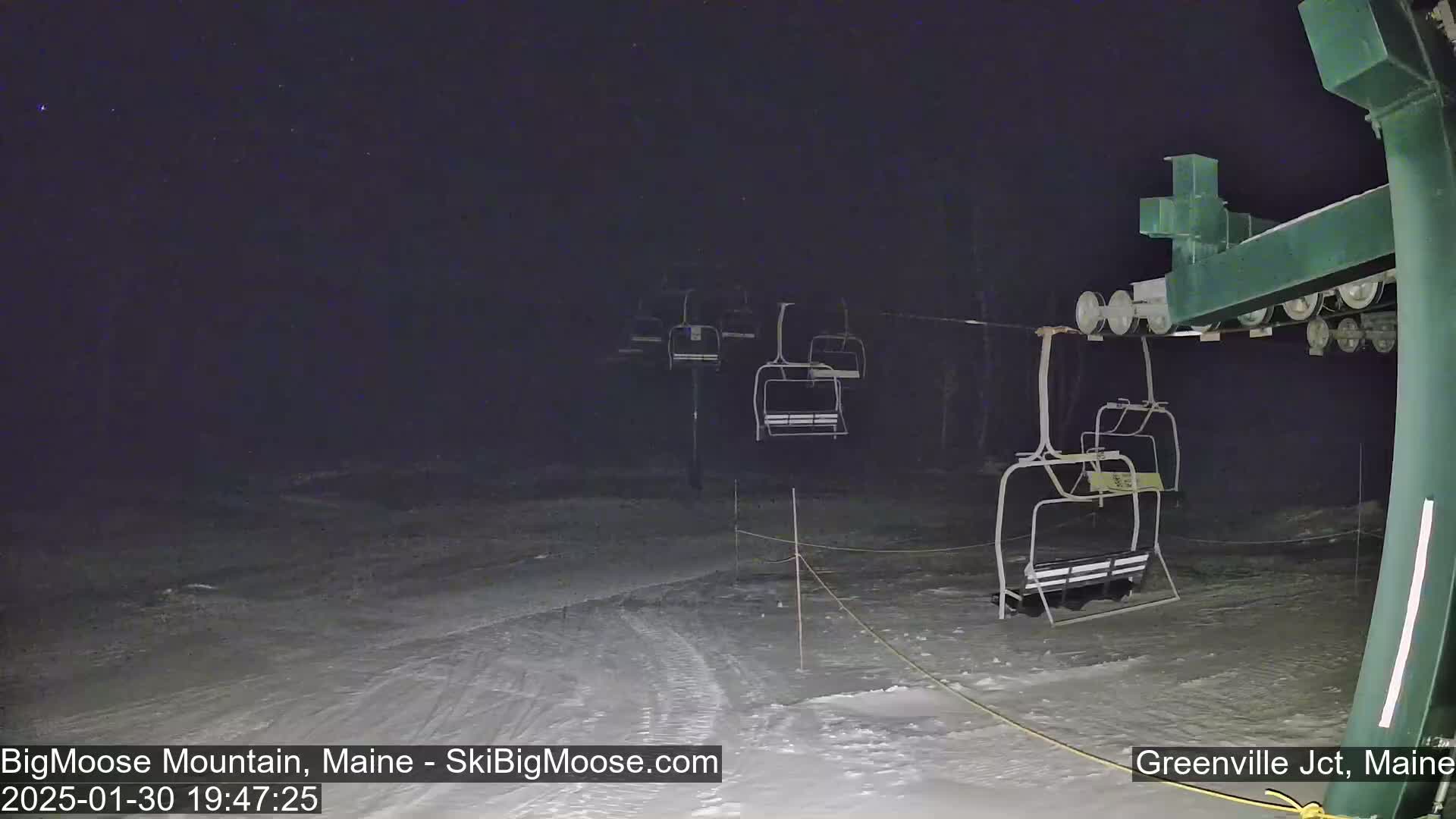 A nighttime view of a snow-covered ski lift with several empty chairs under a clear, starry sky.