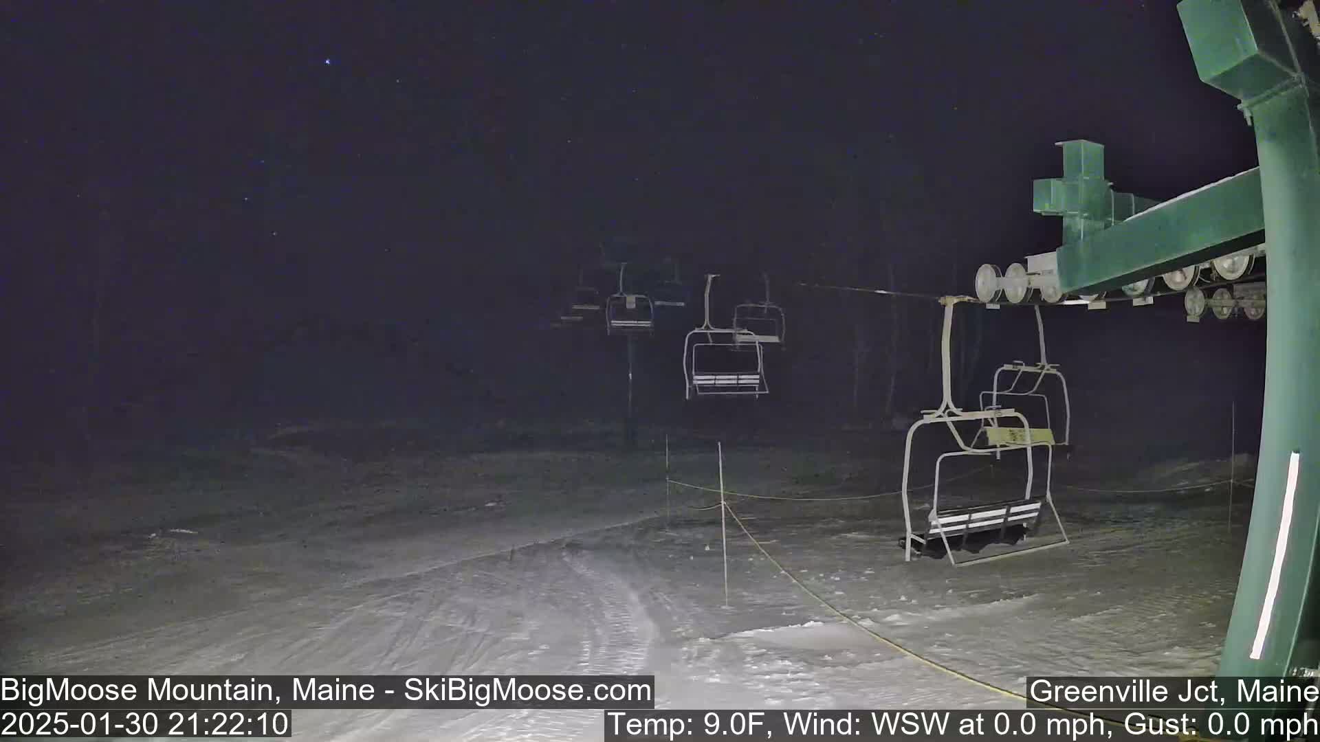A nighttime view of a ski lift with empty chairs under a clear, starry sky.