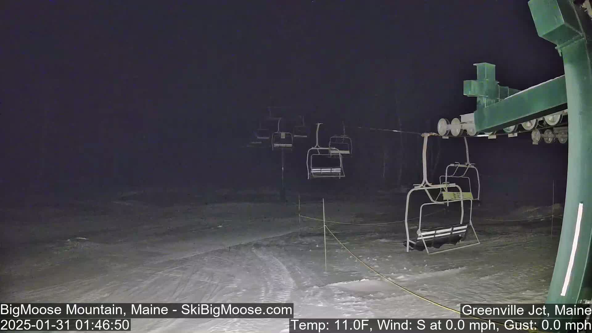 A nighttime view of a ski lift with empty chairs on a snow-covered slope under a dark sky, with a temperature of 11 degrees Fahrenheit and no wind.