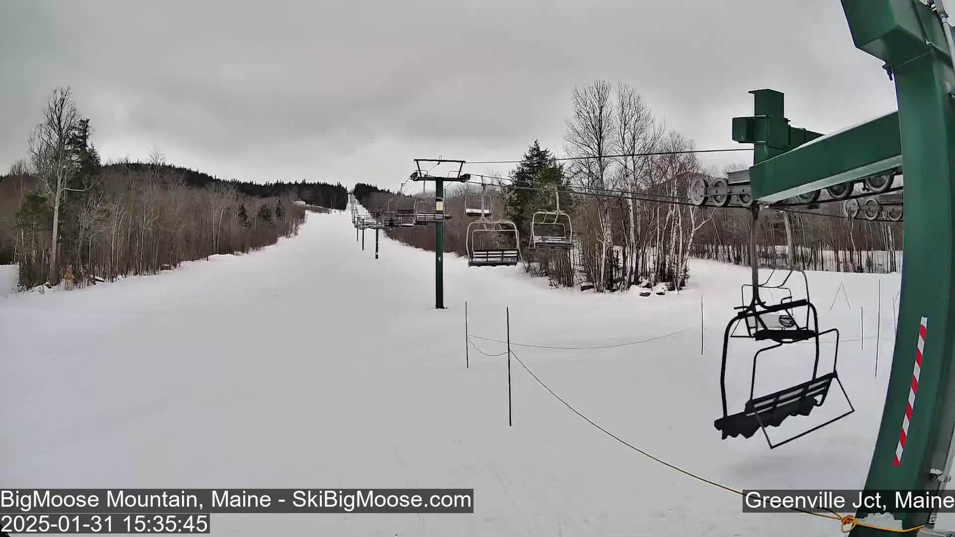 A snow-covered ski slope with a chairlift and bare trees under an overcast sky.