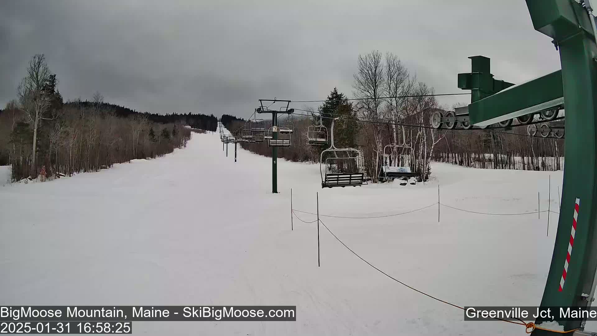 A snow-covered ski slope with a chairlift and bare trees under an overcast sky.