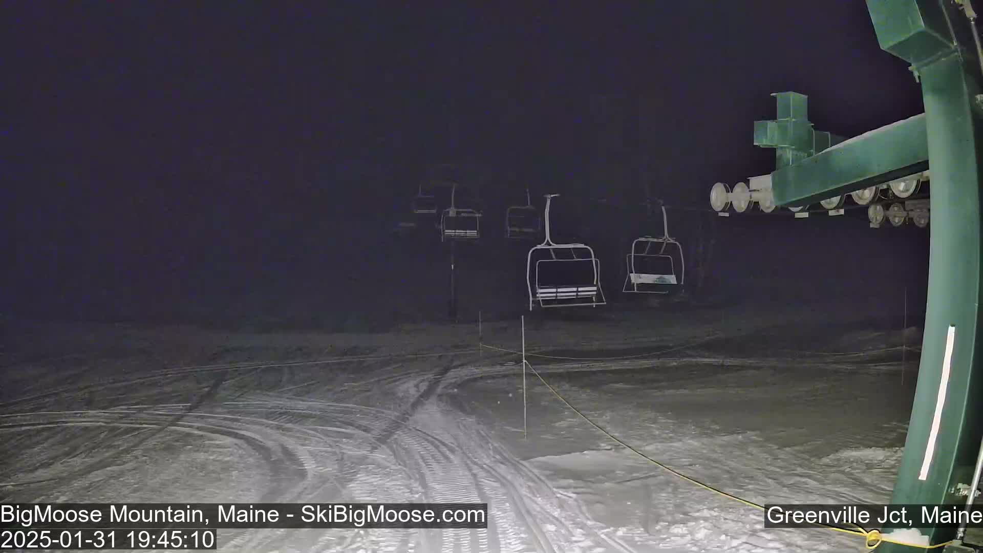 A nighttime view of a ski lift with several empty chairlifts on a snow-covered slope under dark conditions.