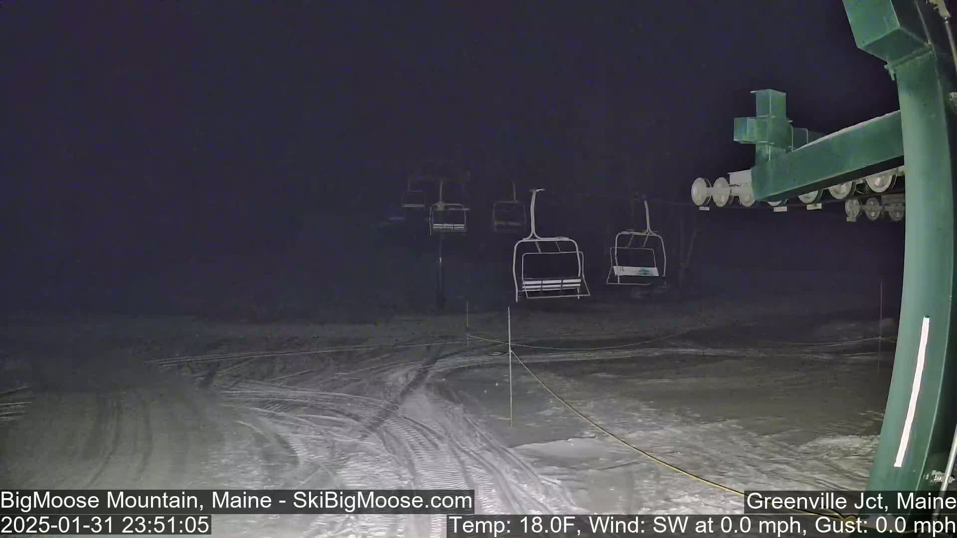 A nighttime view of a snow-covered ski slope with several empty chairlifts under a dark sky.