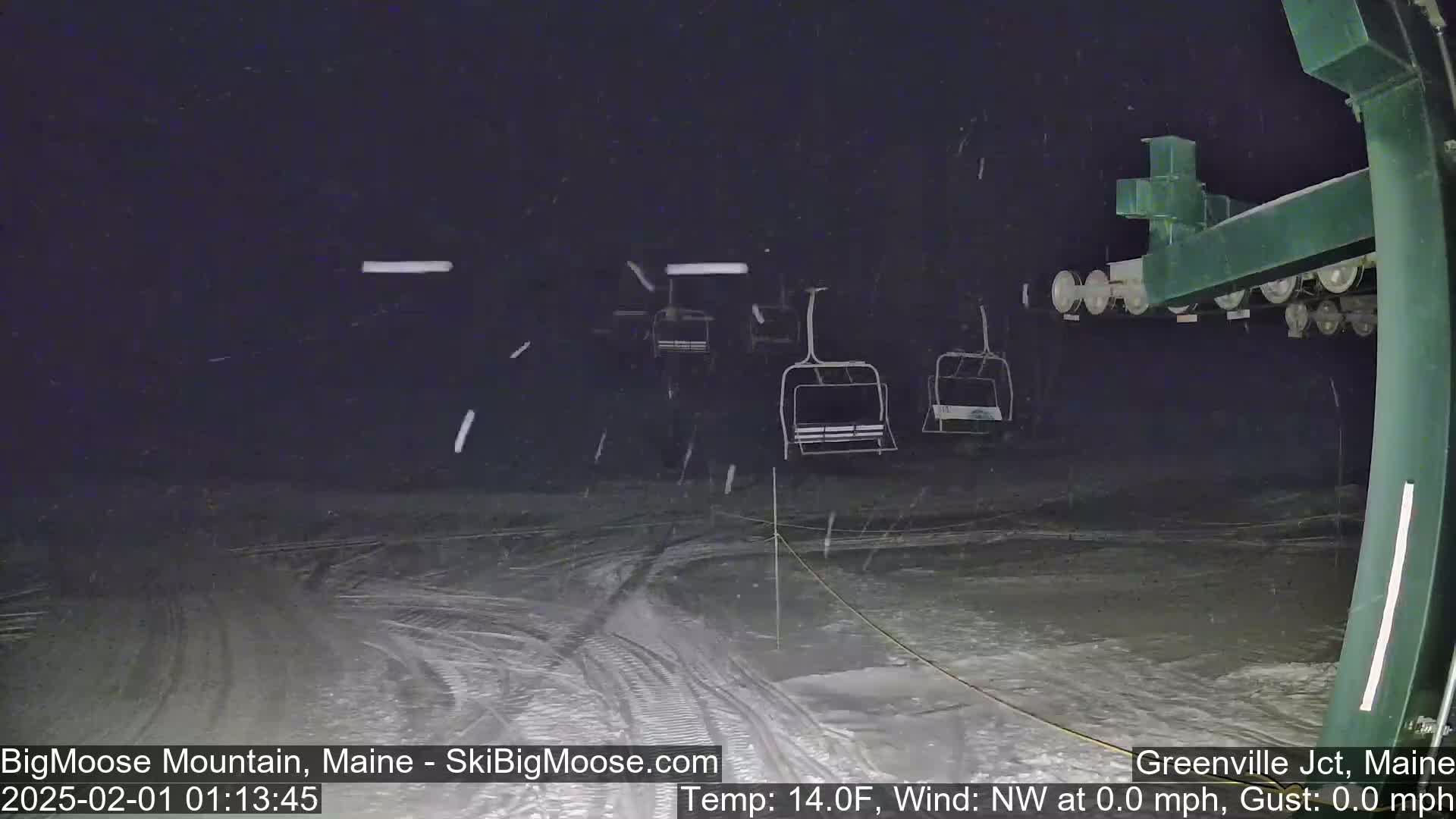 Empty ski lift chairs sit under a nighttime snowfall.