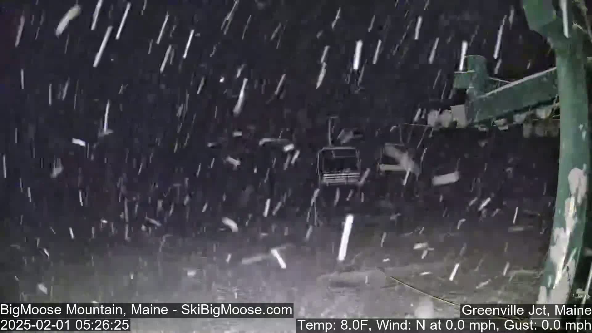 Snow is falling heavily at night, partially obscuring a dark-colored chairlift.