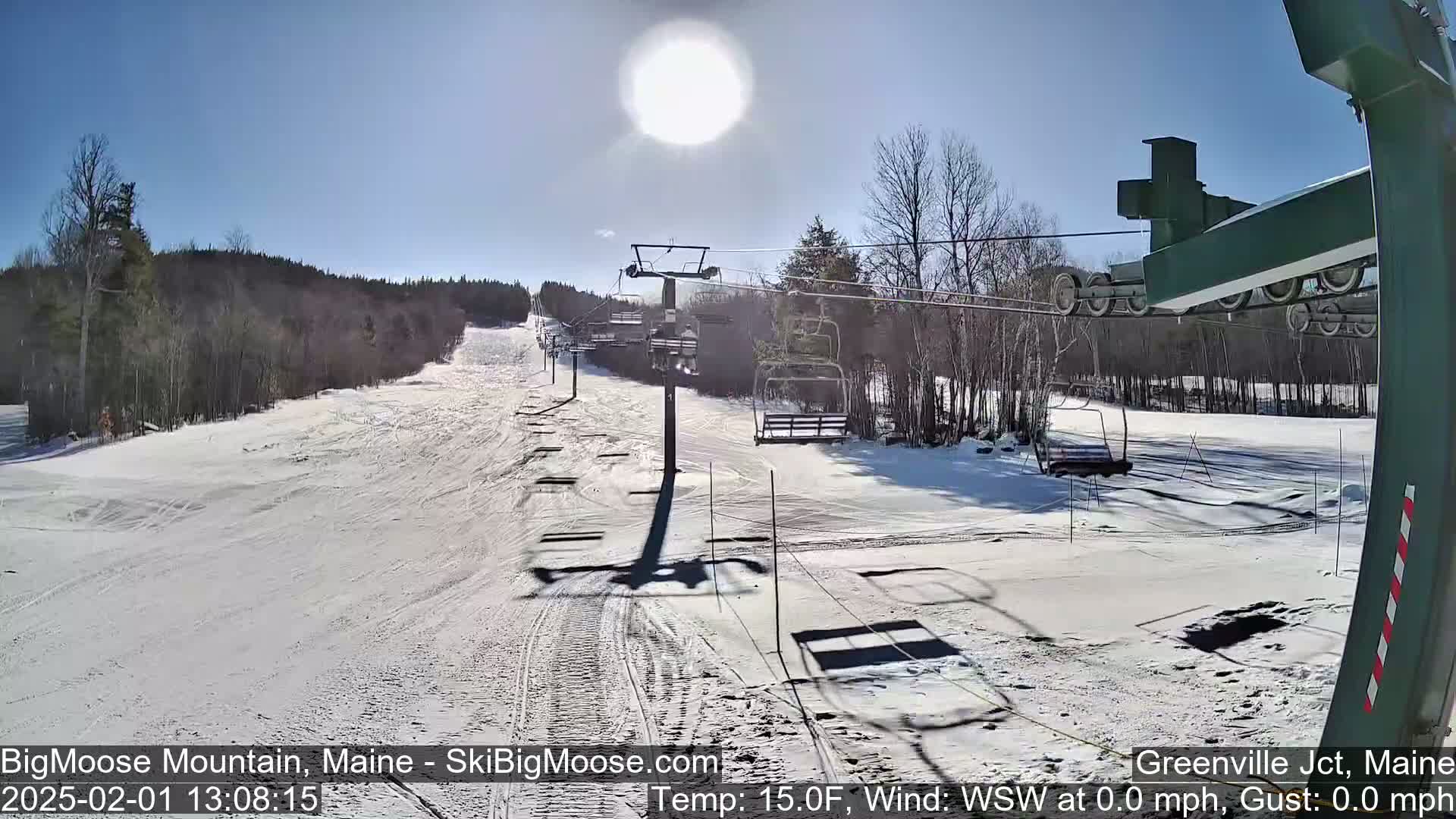 A sunny, snow-covered ski slope with a chairlift and trees in the background.