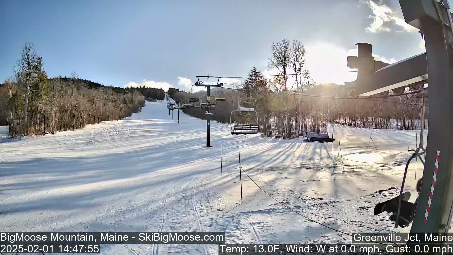 A sunny, snow-covered ski slope with a chairlift and sparse trees under a clear blue sky.