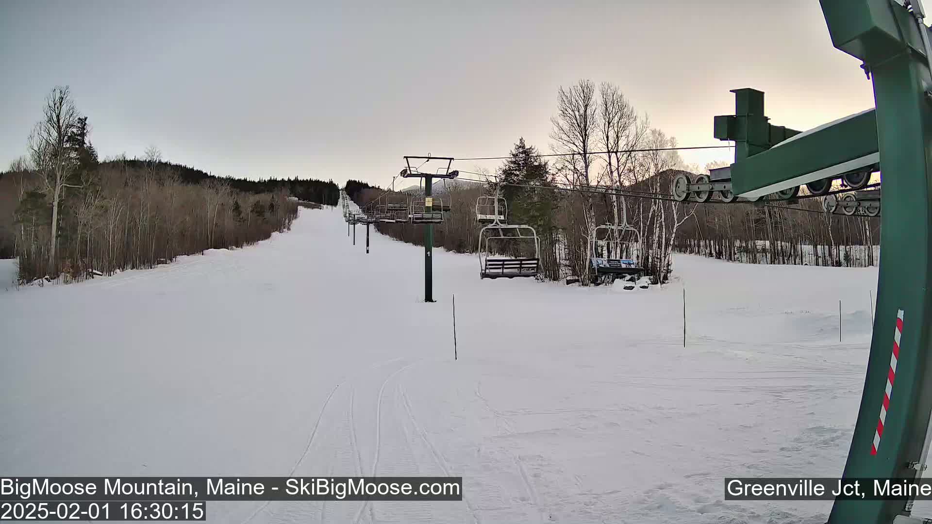 A snow-covered ski slope with a chairlift and bare trees under a mostly clear, dusky sky.