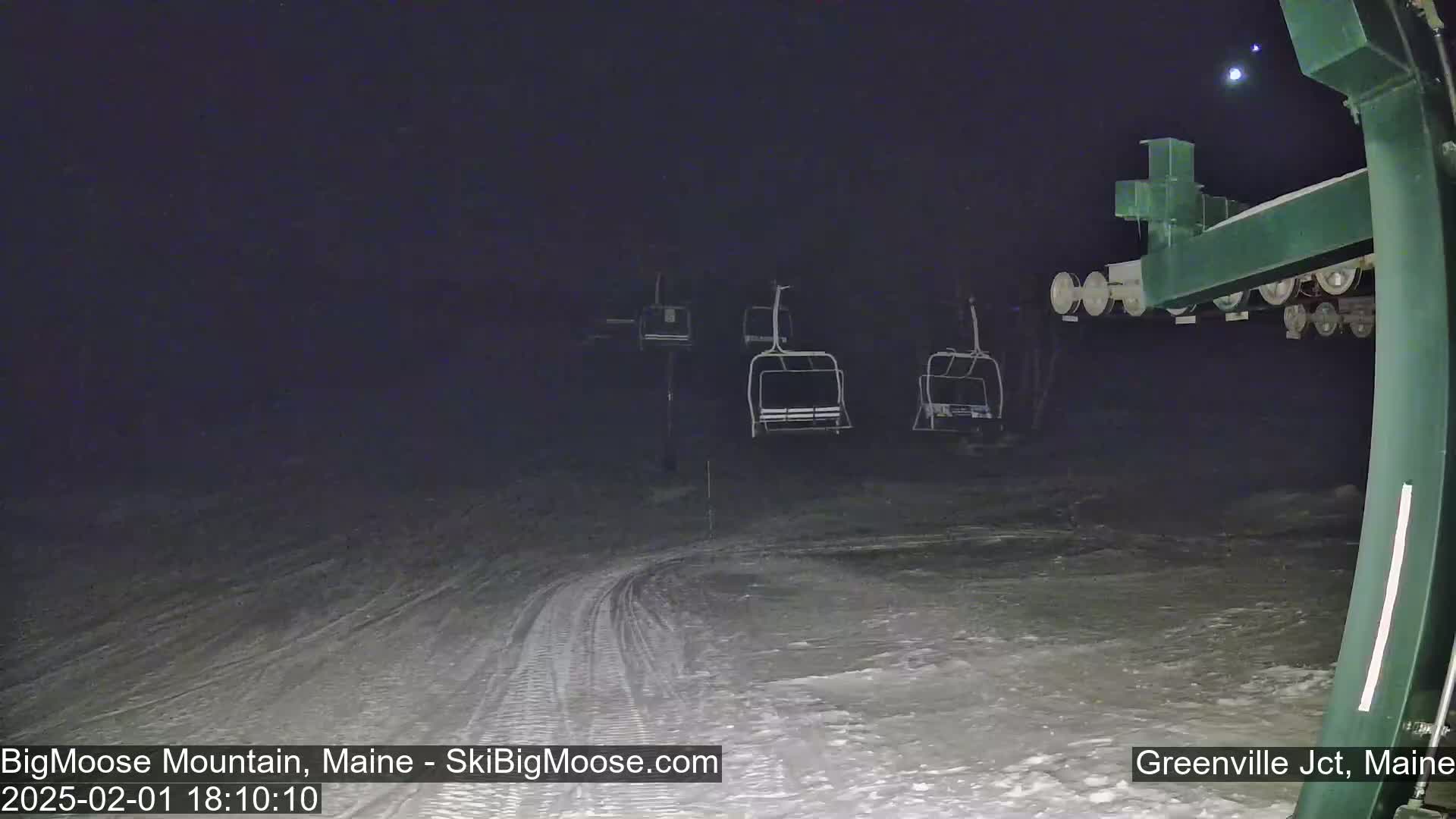 At night, several empty chairlifts are visible on a snow-covered ski slope under a dark sky.
