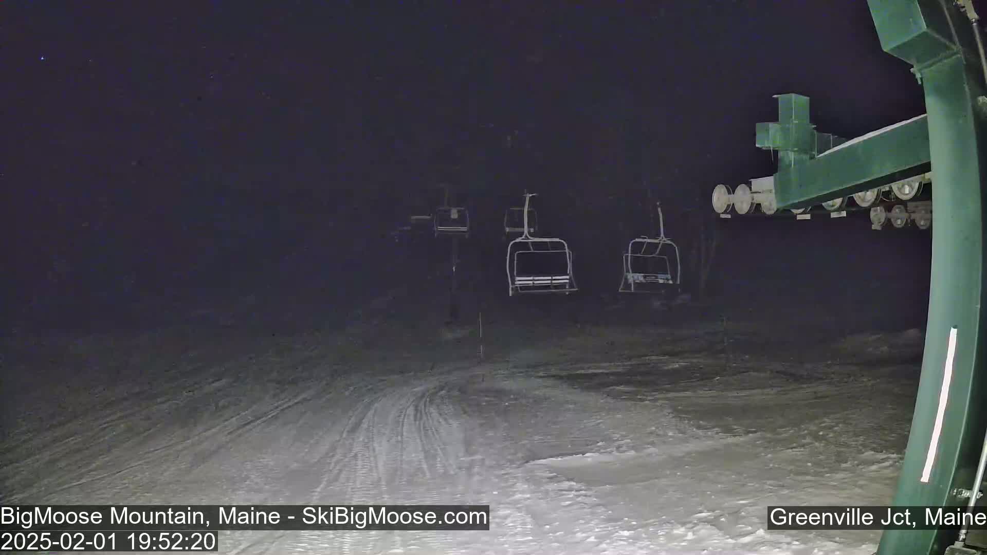 A nighttime view of a snow-covered ski slope with several empty chairlifts visible under a dark, possibly snowy sky.