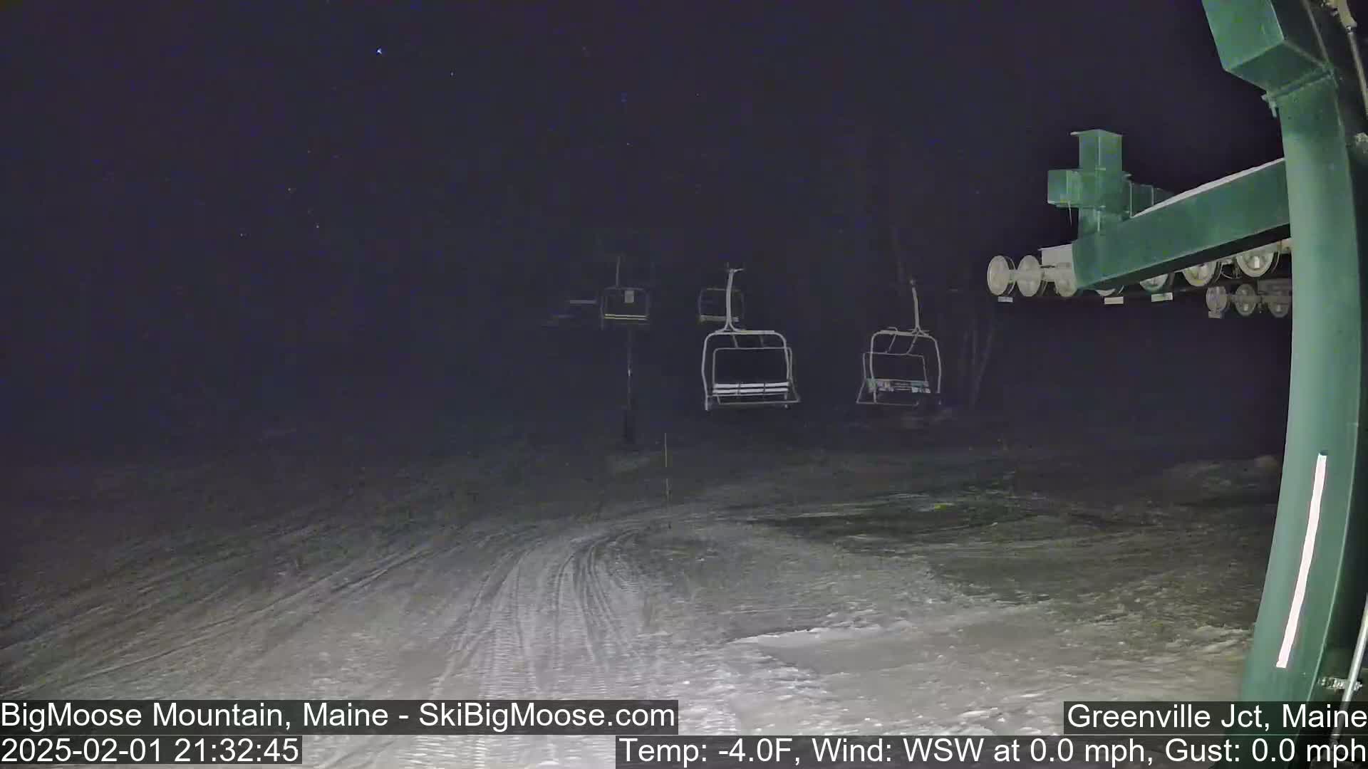 Under a starry night sky, several empty chairlifts sit on a snow-covered ski slope.