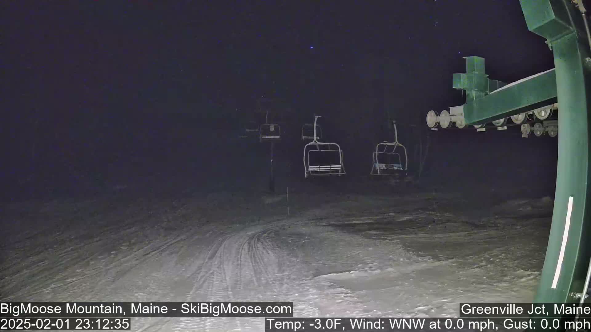 Under a clear, starry night sky, several empty chairlifts are visible on a snow-covered ski slope.