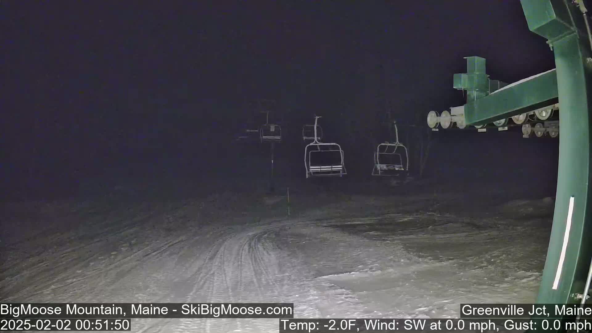 A nighttime view of a snow-covered ski slope with empty chairlifts under a dark sky and calm, cold weather.