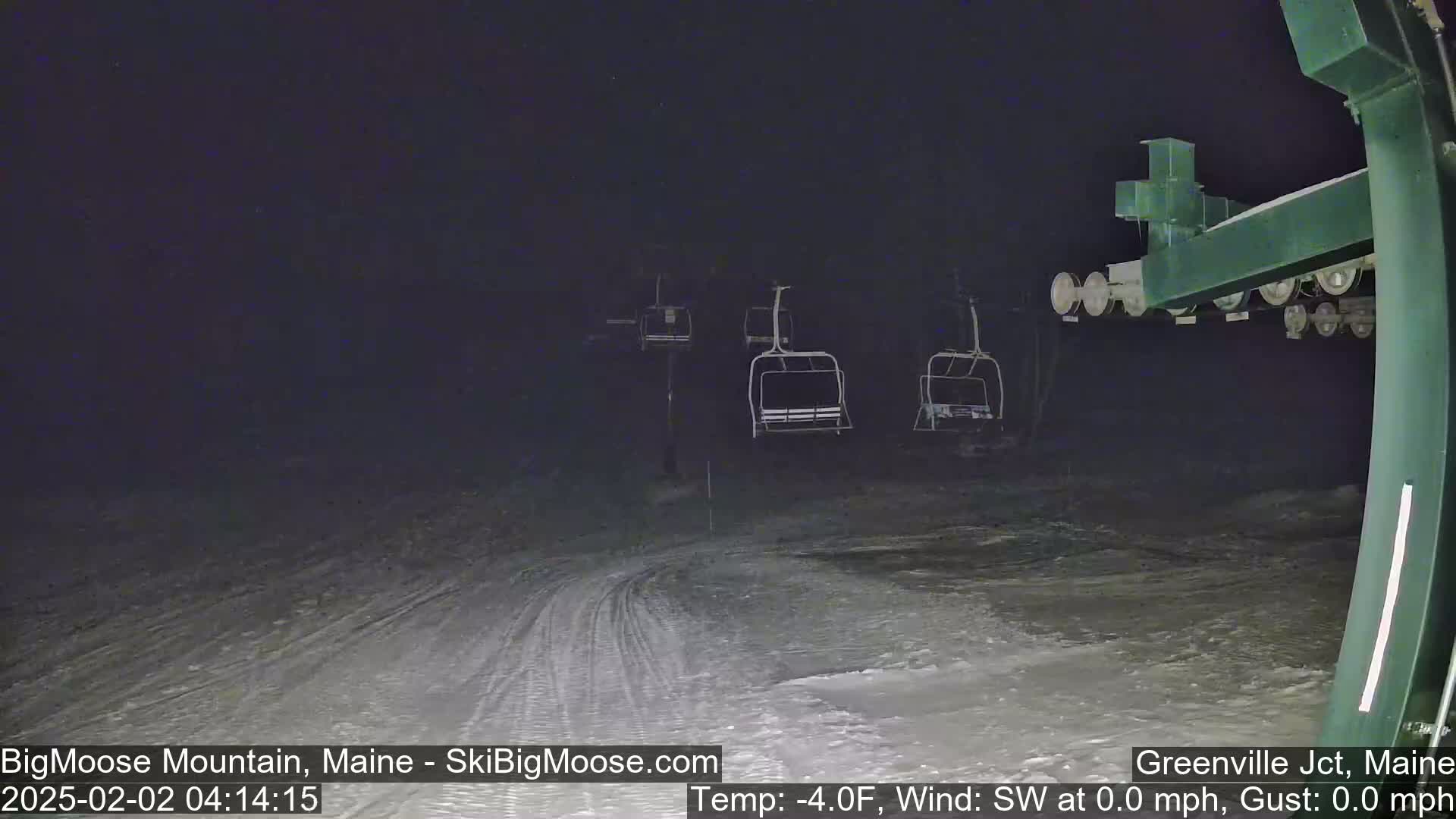 A nighttime view of a snow-covered ski slope with several empty chairlifts under a dark sky.