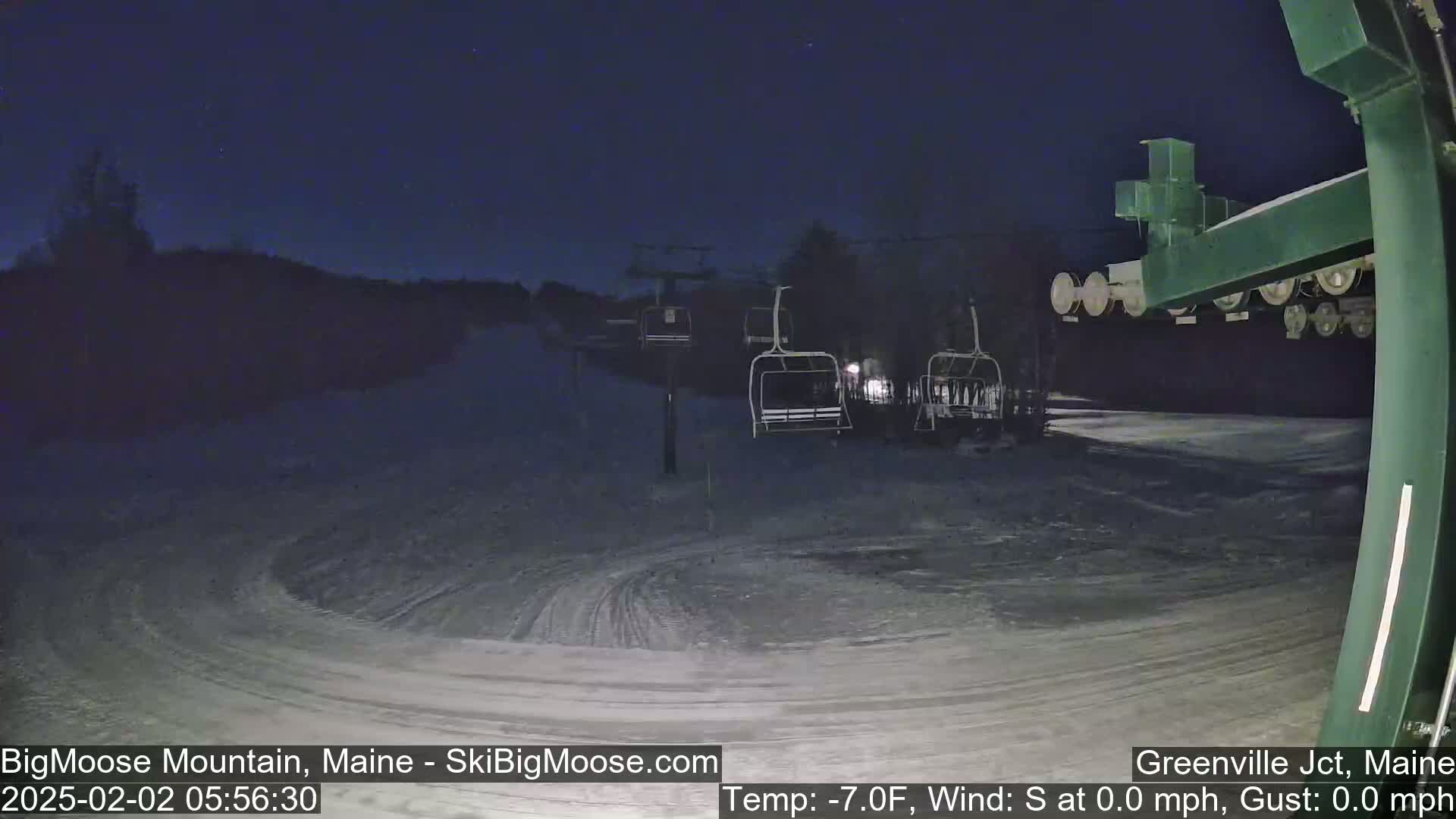 A nighttime view of a snow-covered ski slope with empty chairlifts under a clear, dark sky.