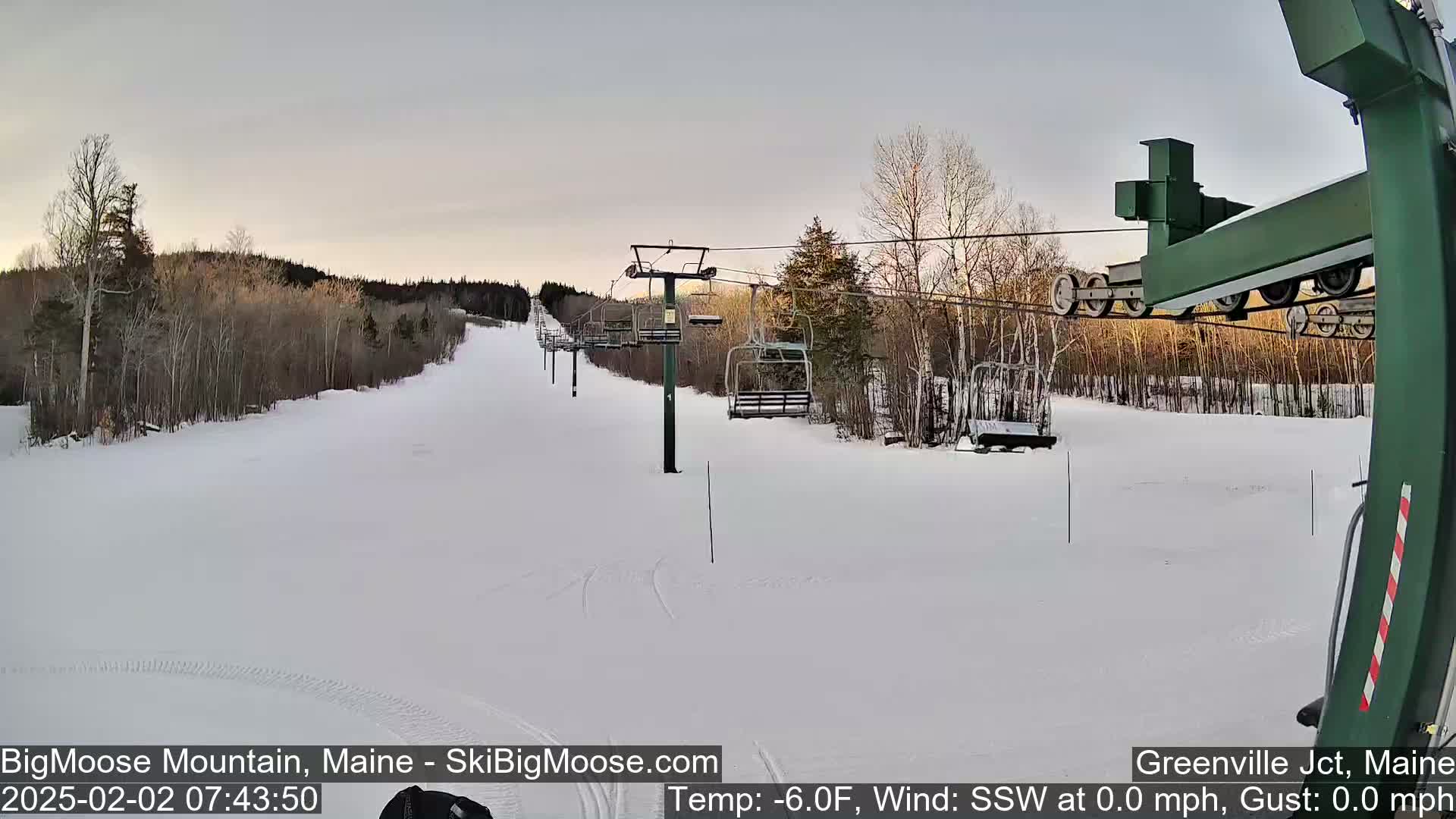 A snow-covered ski slope with a chairlift and bare trees under a pale sky.