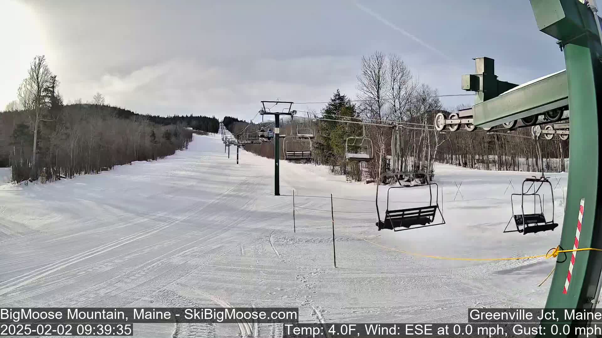 A mostly cloudy day at a ski resort shows a snow-covered ski slope with a chairlift and several empty chairs.