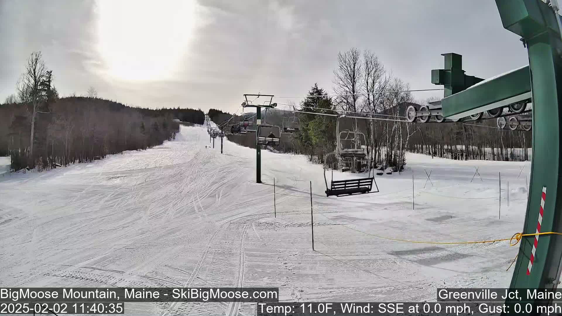 A mostly cloudy, cold day on a snow-covered ski slope with a chairlift and sparsely populated trees in the background.