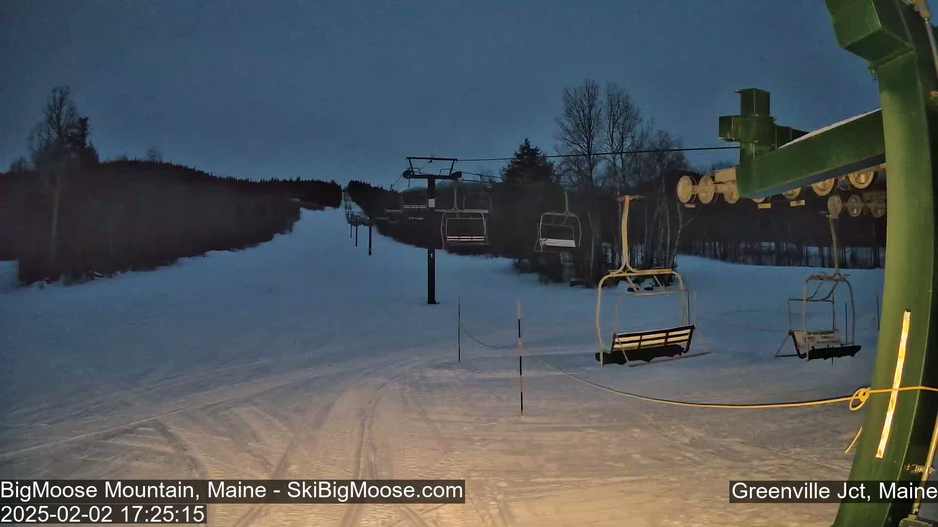 A ski lift with empty chairs stands on a snow-covered slope under a twilight sky.