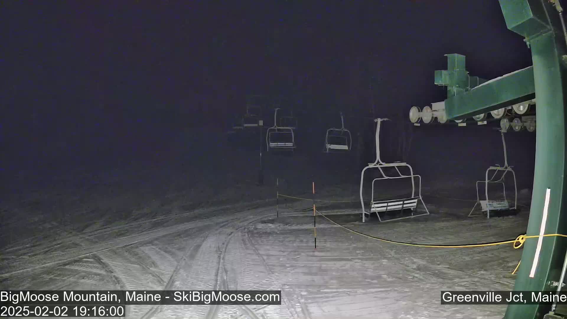A nighttime view of a snow-covered ski slope with several empty chairlifts under a dark sky.