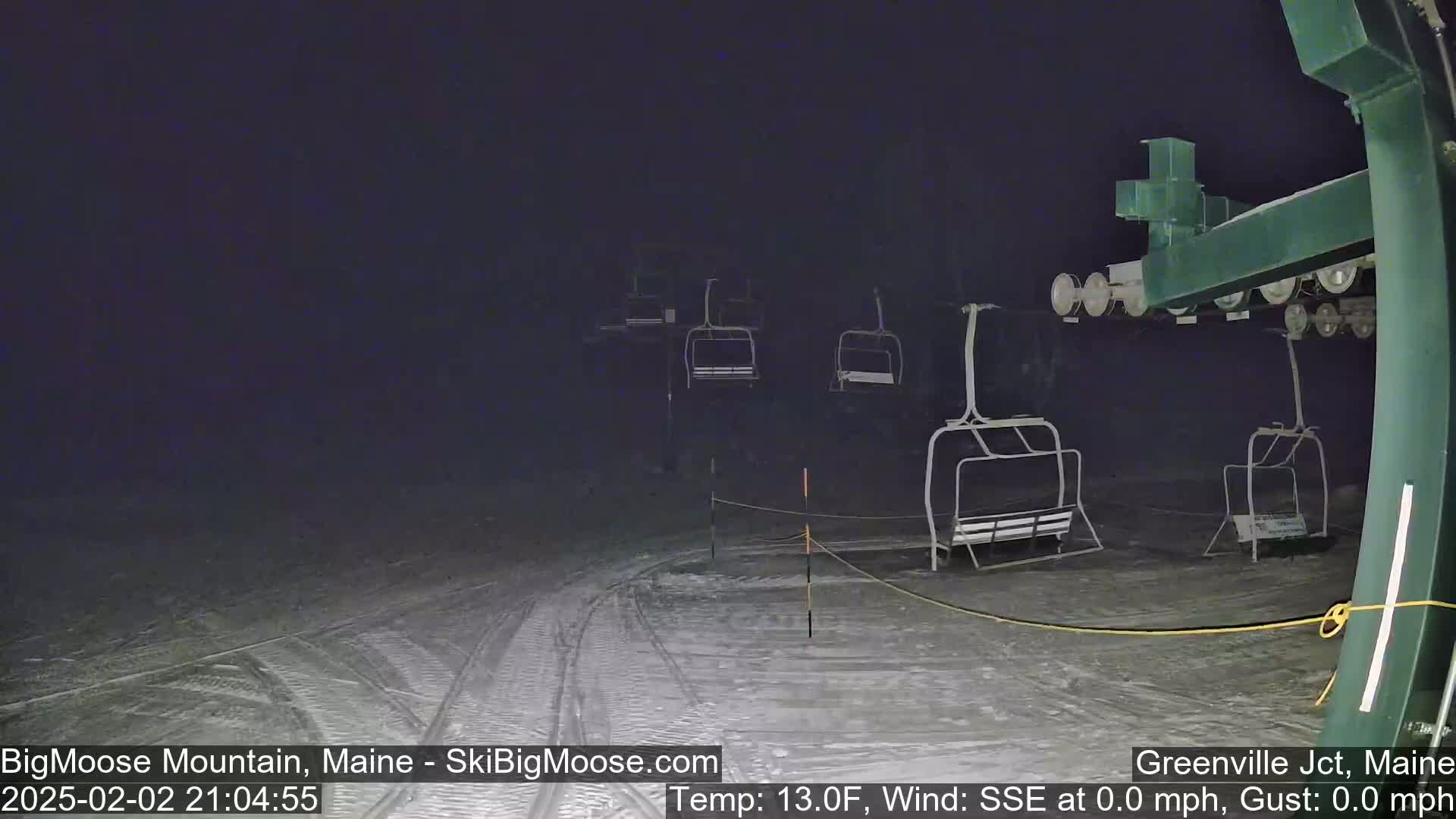 A nighttime view of a ski lift with several empty chairs at a snowy ski resort under dark, clear skies.