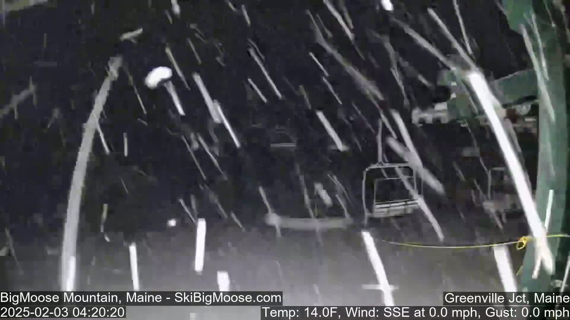 Heavy snowfall obscures a view of a chairlift during nighttime.