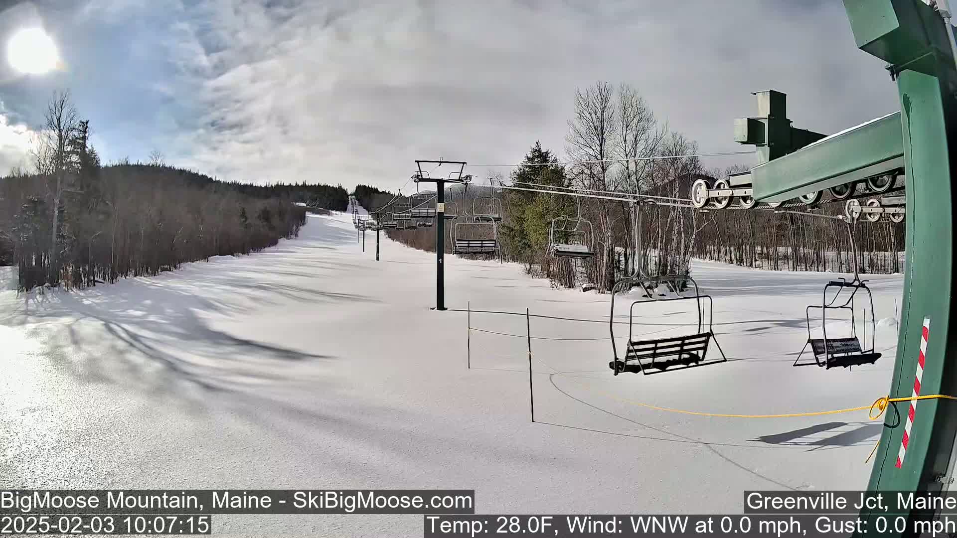 A snow-covered ski slope with empty chairlifts under a partly sunny sky.