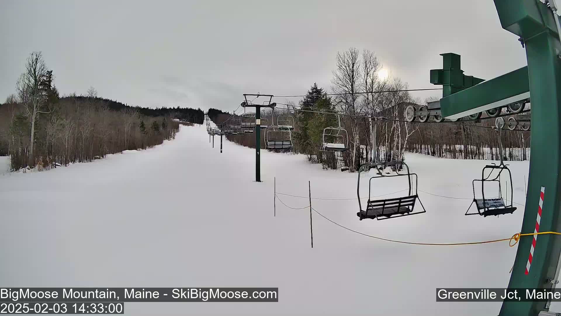 A snow-covered ski slope with a chairlift and sparsely wooded areas under an overcast sky.