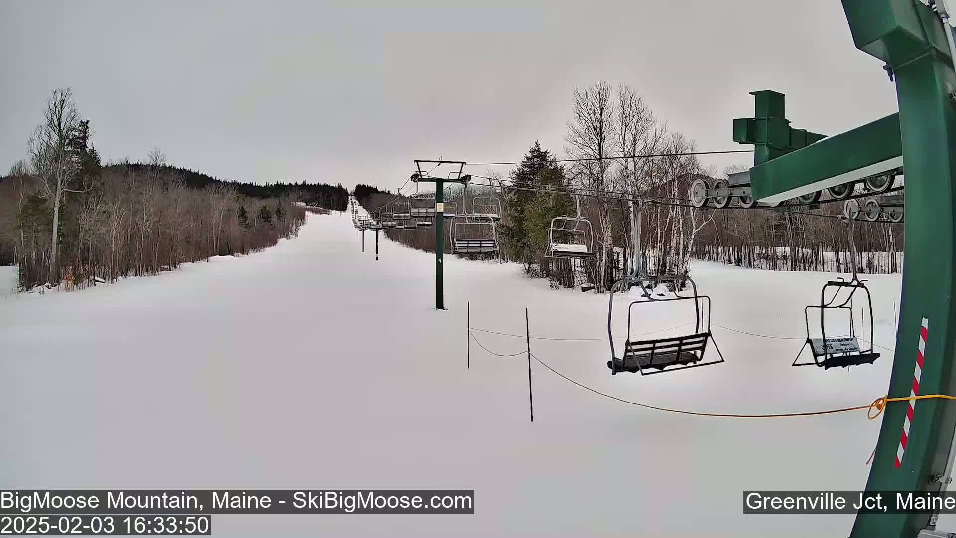 A snowy ski slope with a chairlift and bare trees under an overcast sky.