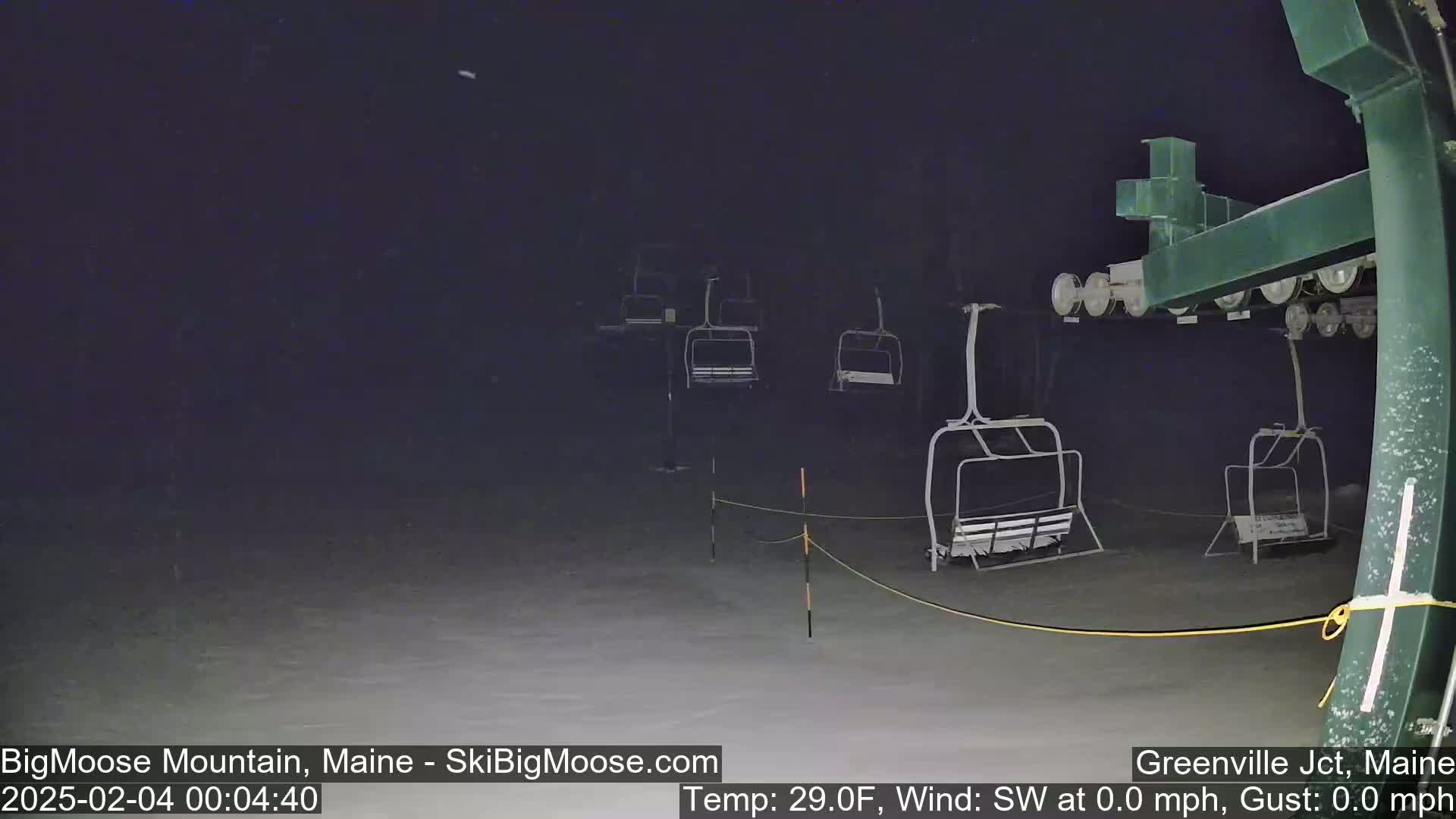 A nighttime view of empty ski lift chairs on a snow-covered surface during calm, cold conditions.